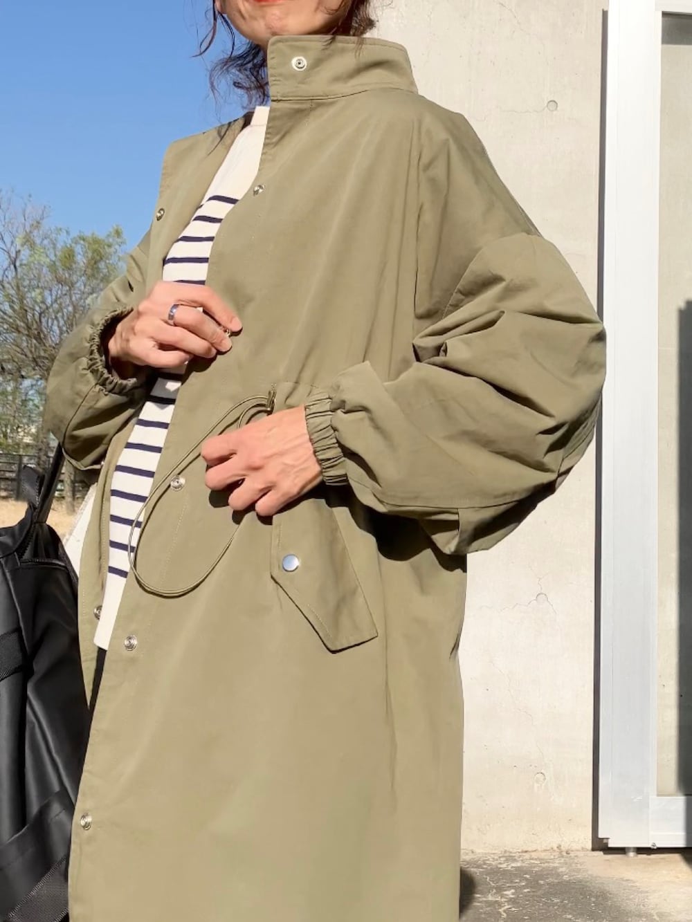 グリーン系のステンカラーコート、ブラック系のバックパック/リュック、ブラウン系のブーツを着用したレディースの秋コーディネートの3枚目の写真