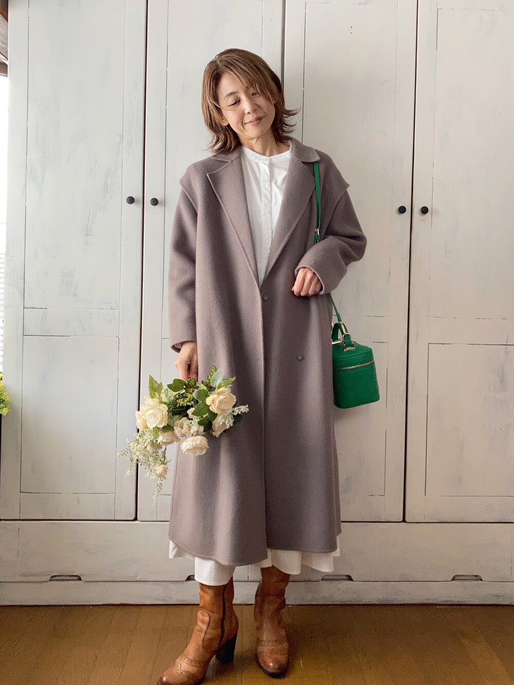 ブラウン系のチェスターコート、ホワイト系のワンピース/ドレス、グリーン系のショルダーバッグを着用したレディースの冬コーディネートの2枚目の写真