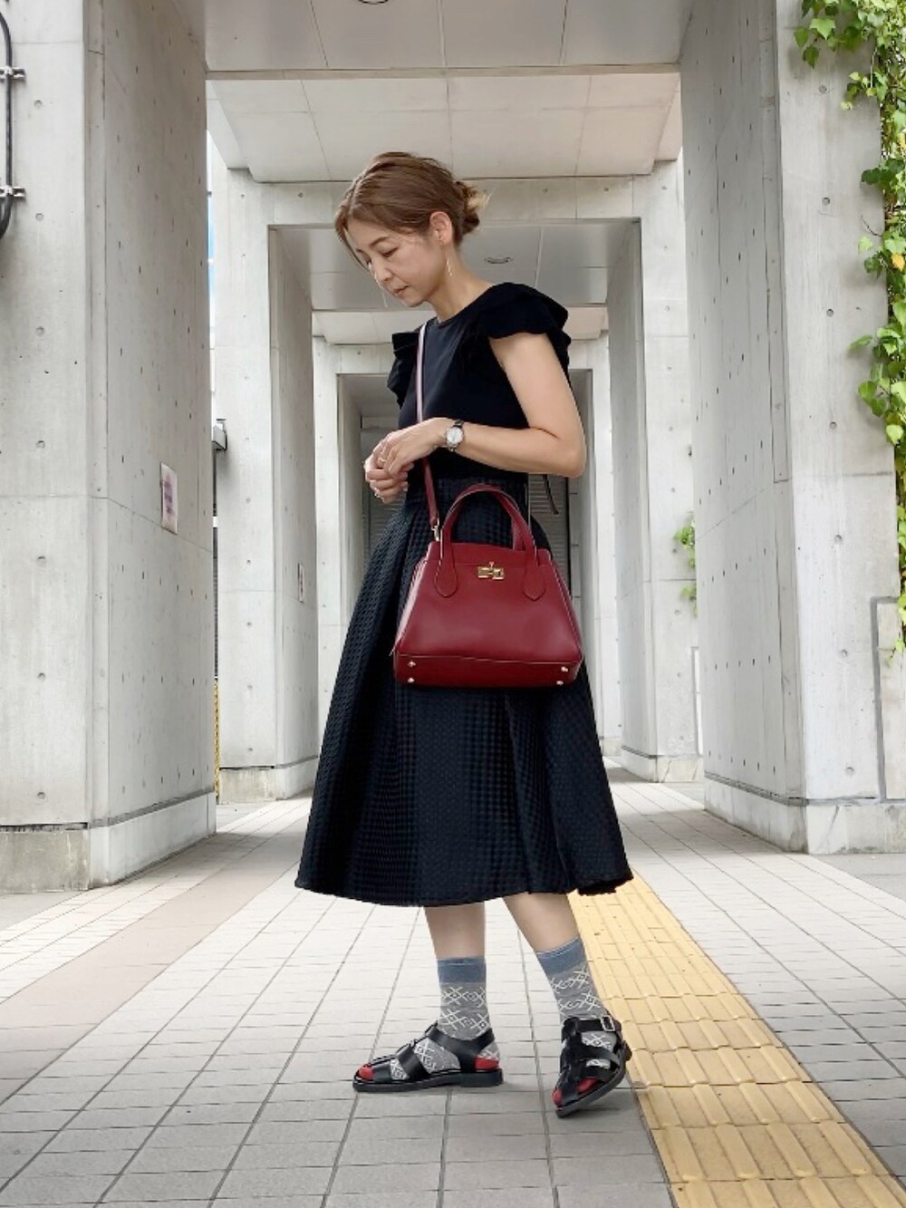 ブラック系のニット/セーター、ブラック系のスカート、レッド系のハンドバッグを着用したレディースの夏コーディネートの2枚目の写真
