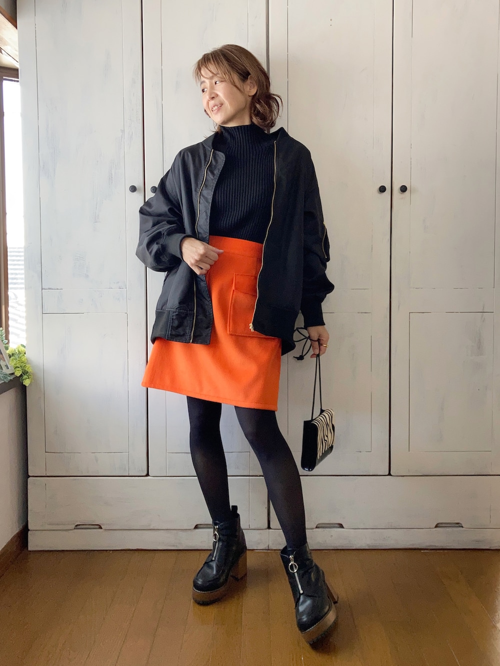 ブラック系のブルゾン、ブラック系のニット/セーター、オレンジ系のスカートを着用したレディースの冬コーディネートの2枚目の写真