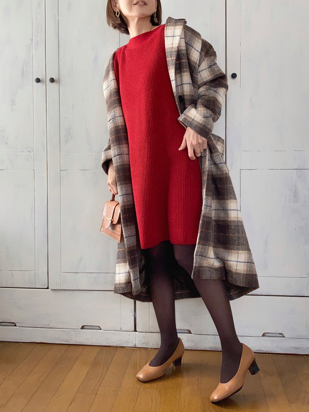 レッド系のワンピース、ブラウン系のチェスターコート、ベージュ系のパンプスを着用したレディースの冬コーディネートの2枚目の写真