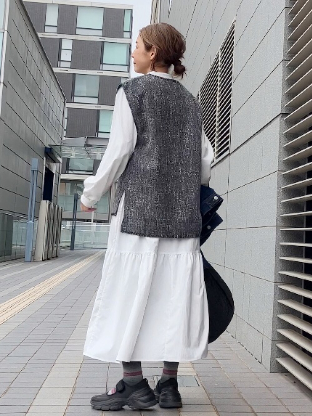 グレー系のベスト、ブルー系のデニムジャケット、ホワイト系のワンピース/ドレスを着用したレディースの春コーディネートの3枚目の写真