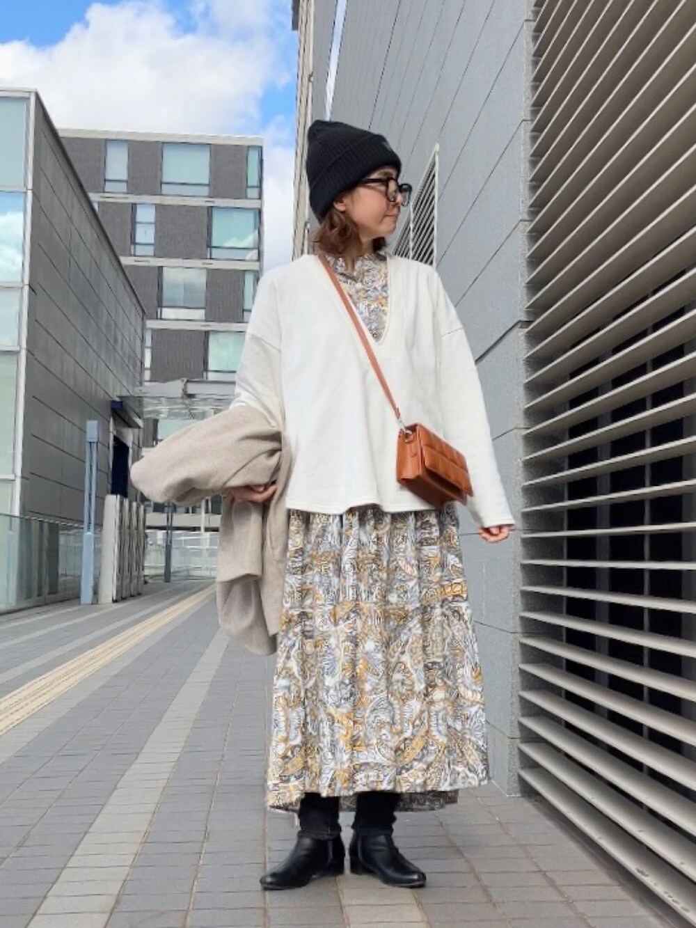 イエロー系のワンピース、ブラウン系のクラッチバッグ、ブラック系のブーツを着用したレディースの冬コーディネートの2枚目の写真