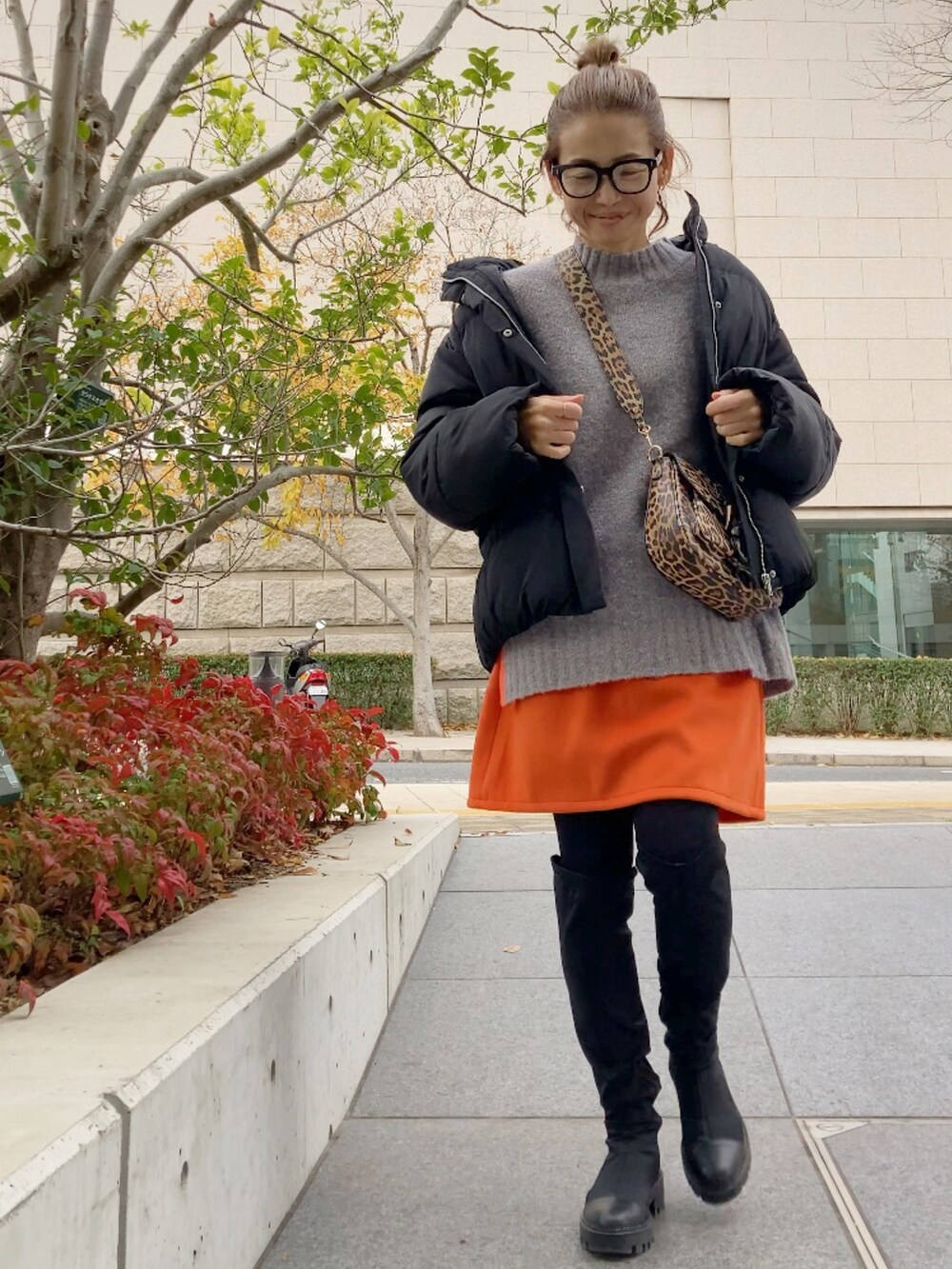 グレー系のニット/セーター、ブラック系のダウンジャケット/コート、オレンジ系のスカートを着用したレディースの冬コーディネートの2枚目の写真