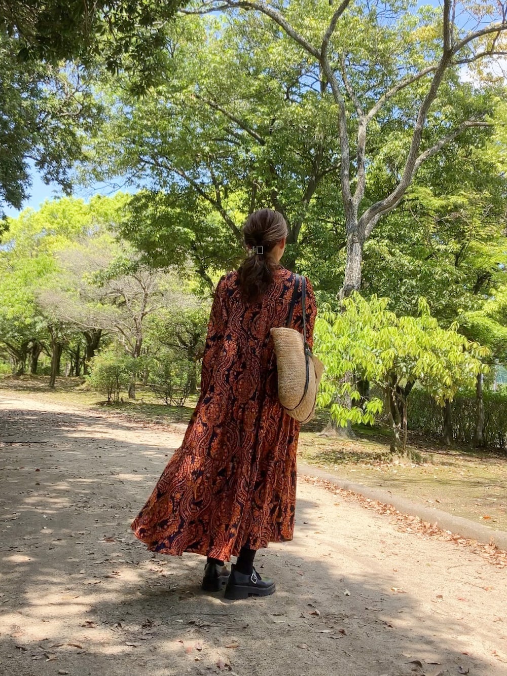 オレンジ系のワンピース、ベージュ系のバッグ、ブラック系のシューズを着用したレディースの春コーディネートの2枚目の写真