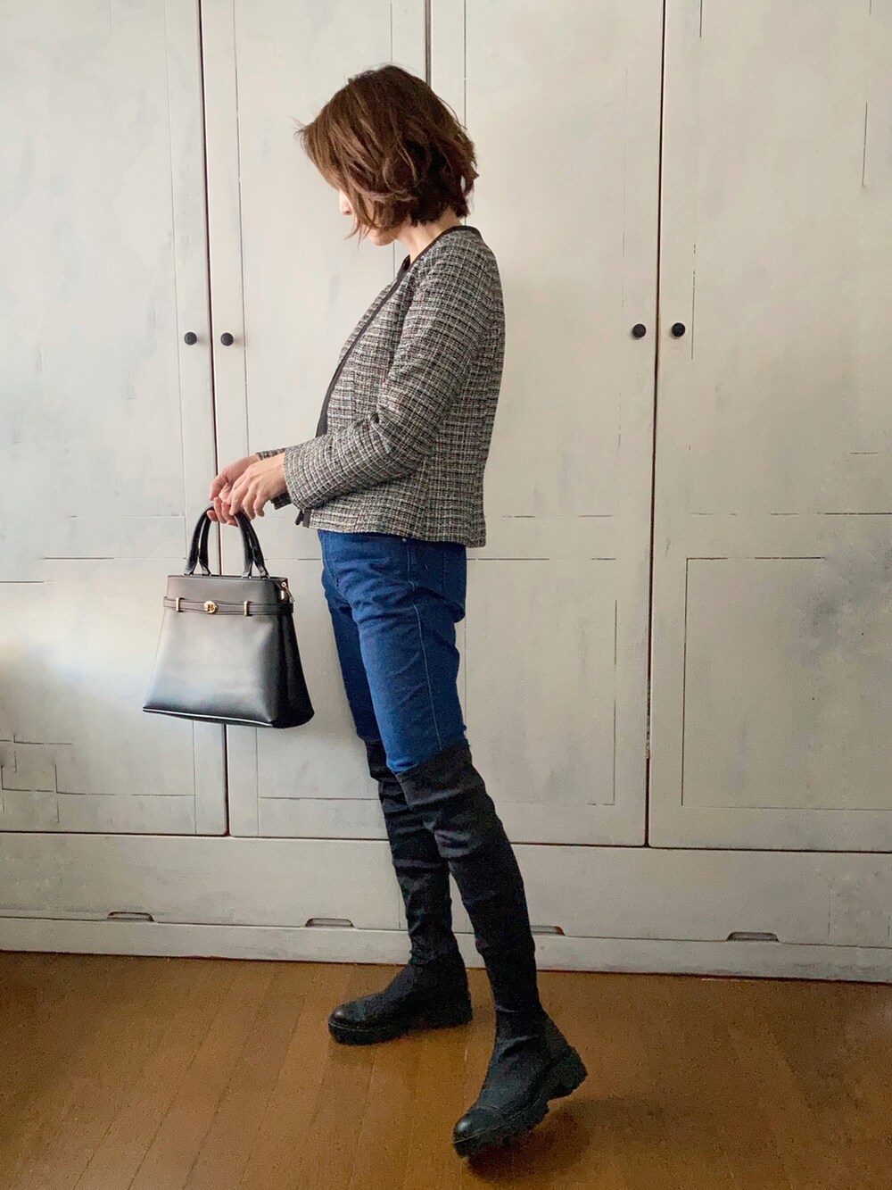 ブラック系のスーツセット、ブラック系のハンドバッグ、ブルー系のデニムパンツを着用したレディースの冬コーディネートの2枚目の写真