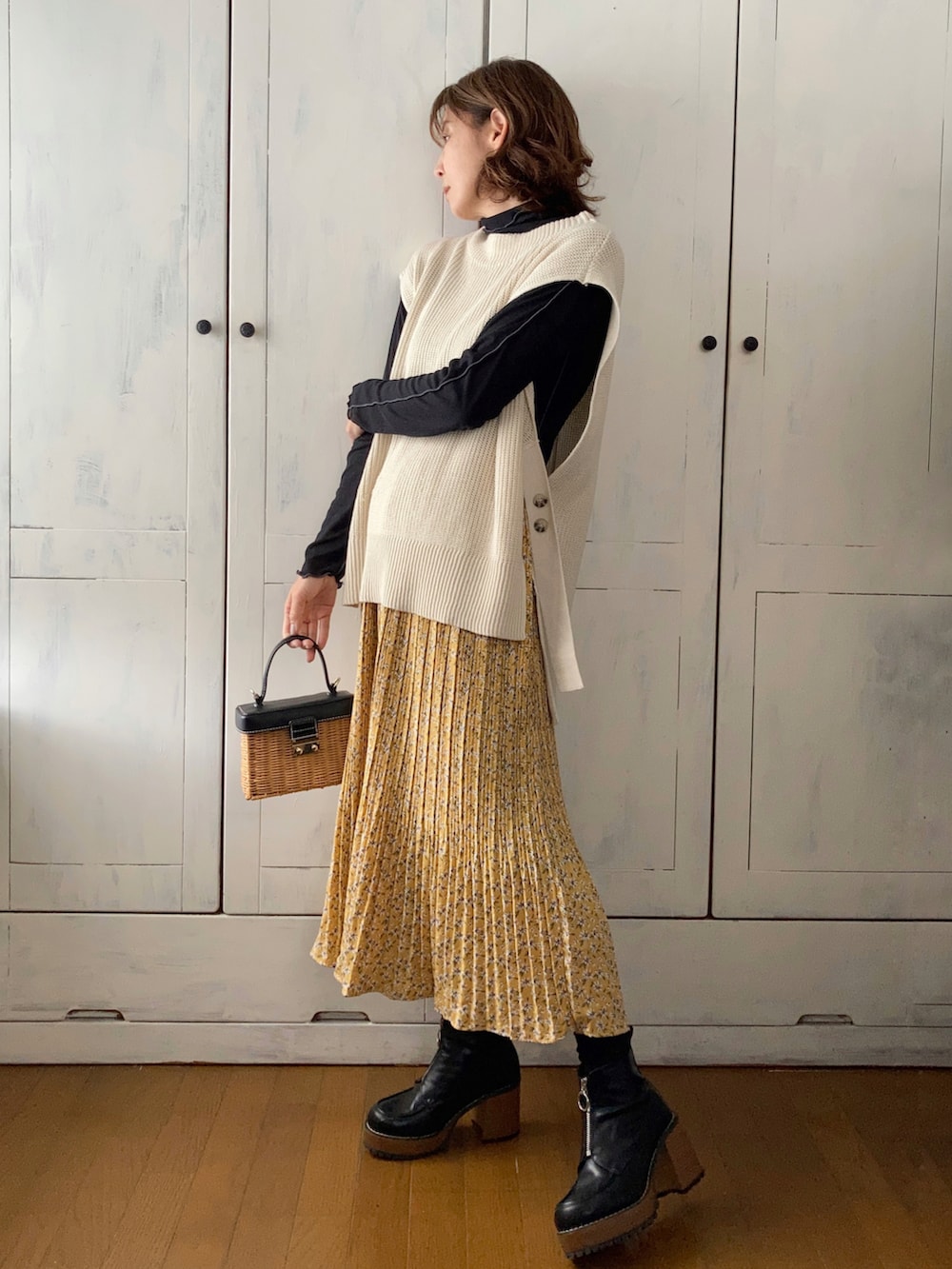 ホワイト系のベスト、イエロー系のスカート、ブラウン系のかごバッグを着用したレディースの春コーディネートの2枚目の写真