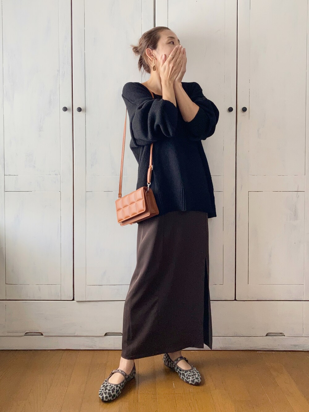 ブラック系のニット/セーター、ブラウン系のワンピース、ブラウン系のクラッチバッグを着用したレディースの秋コーディネートの2枚目の写真