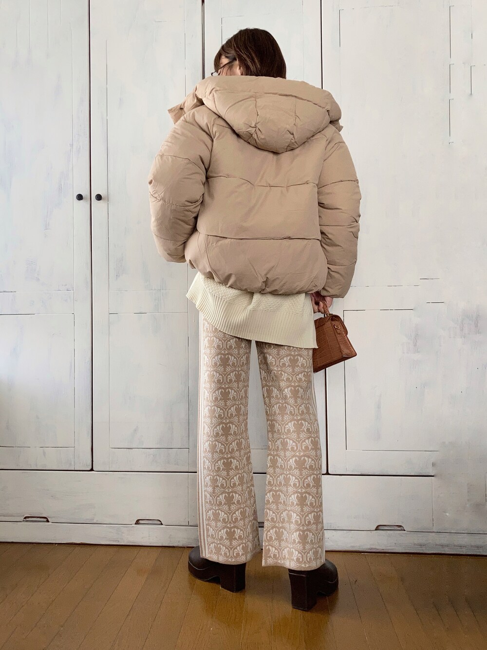 ベージュ系のダウンジャケット/コート、ホワイト系のカーディガン/ボレロ、ブラウン系のハンドバッグを着用したレディースの秋コーディネートの2枚目の写真