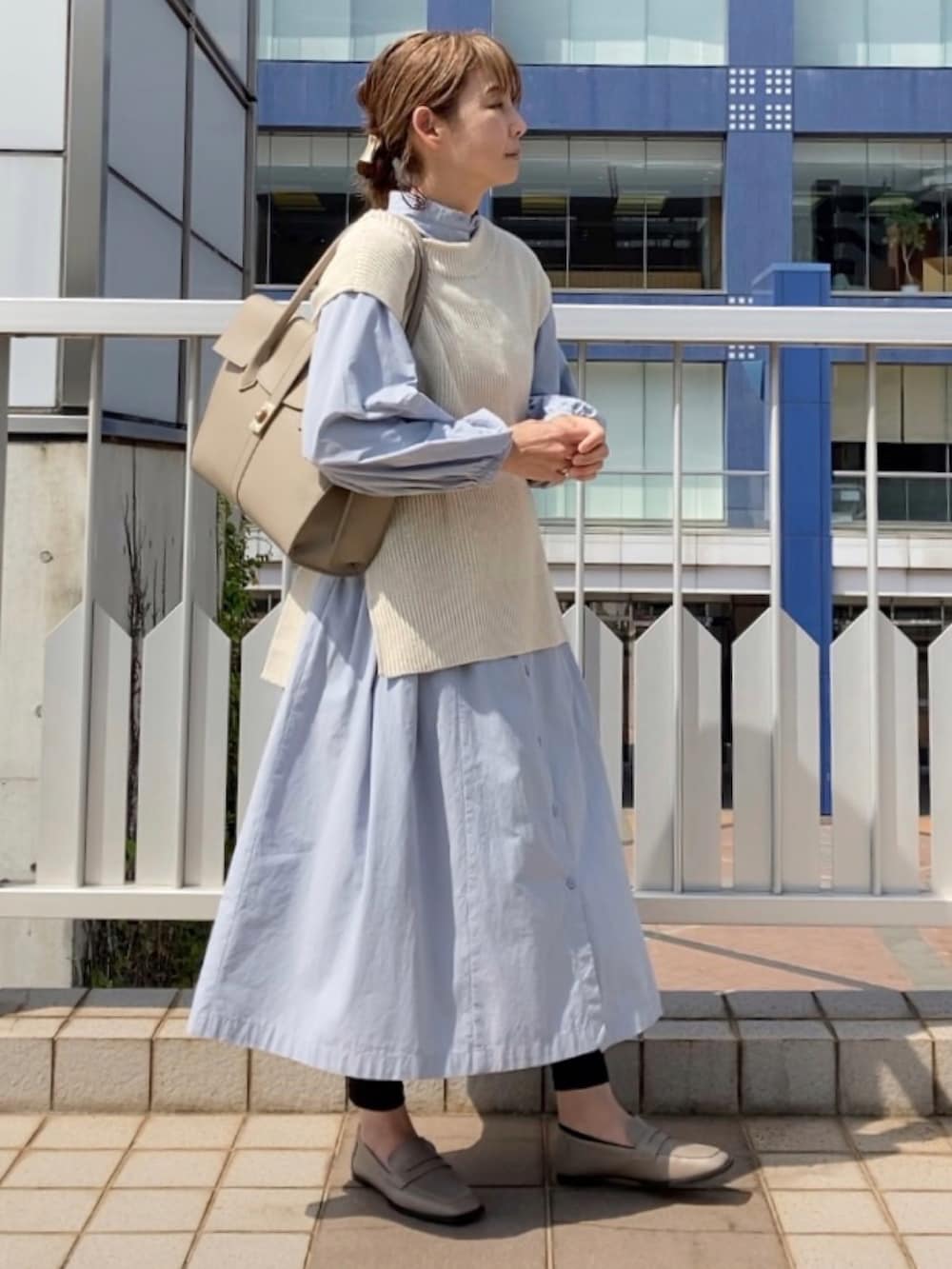ホワイト系のベスト、ブルー系のシャツワンピース、ベージュ系のビジネスバッグを着用したレディースの春コーディネートの2枚目の写真