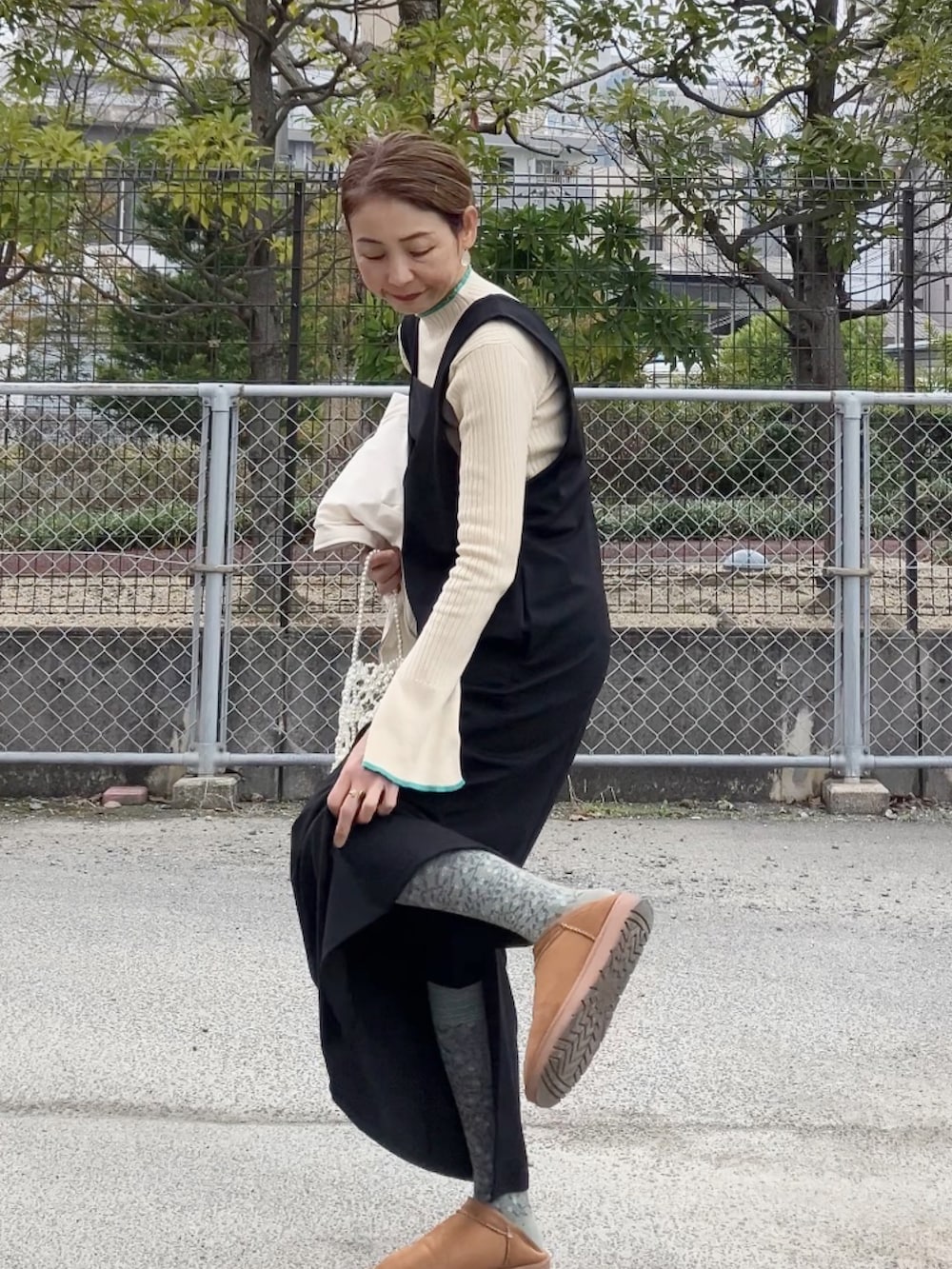 ブラック系のジャンパースカート、ホワイト系のハンドバッグ、イエロー系のサンダルを着用したレディースの冬コーディネートの3枚目の写真