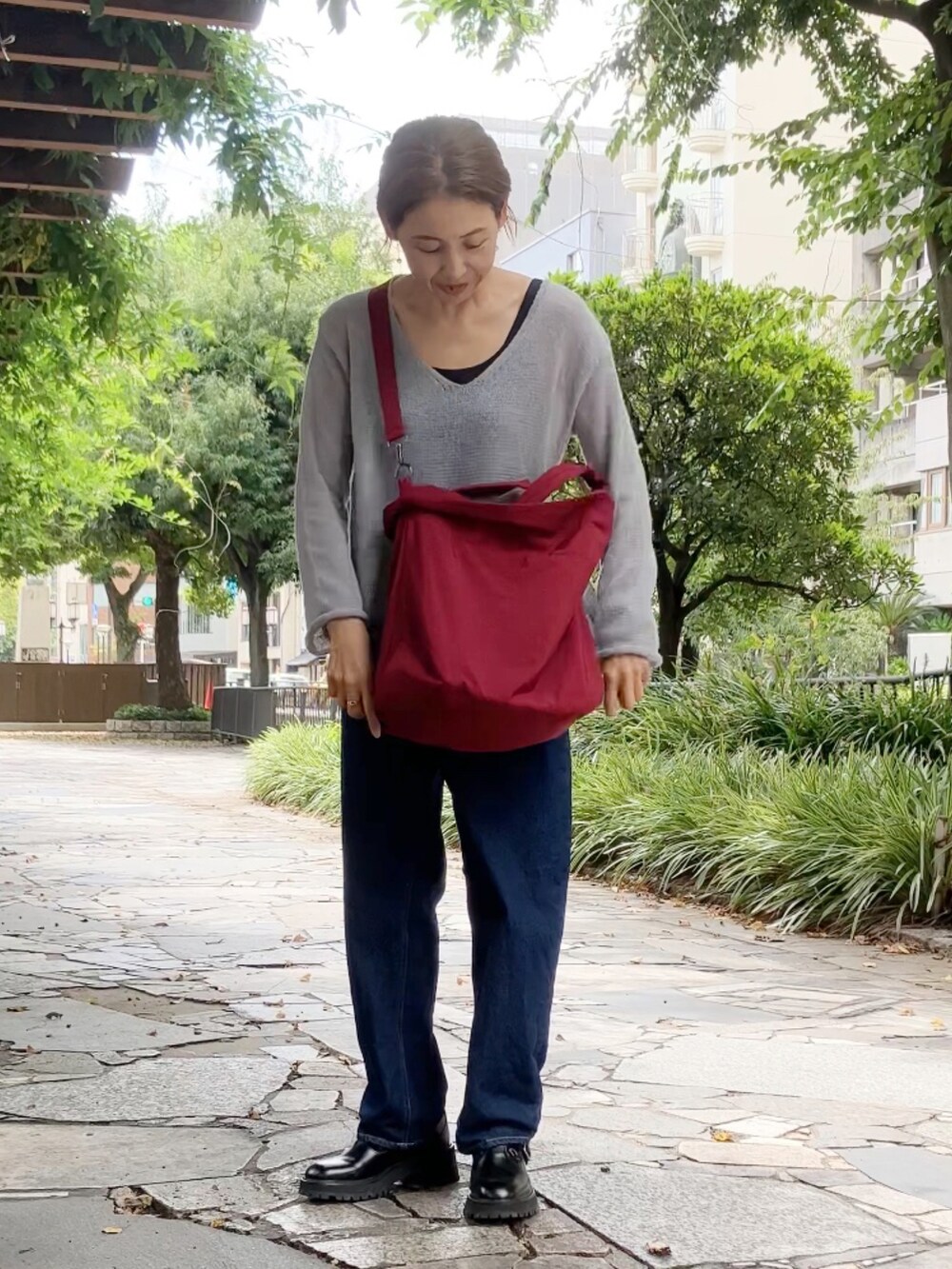 レッド系のボストンバッグ、グレー系のその他トップス、ブルー系のデニムパンツを着用したレディースの秋コーディネートの2枚目の写真