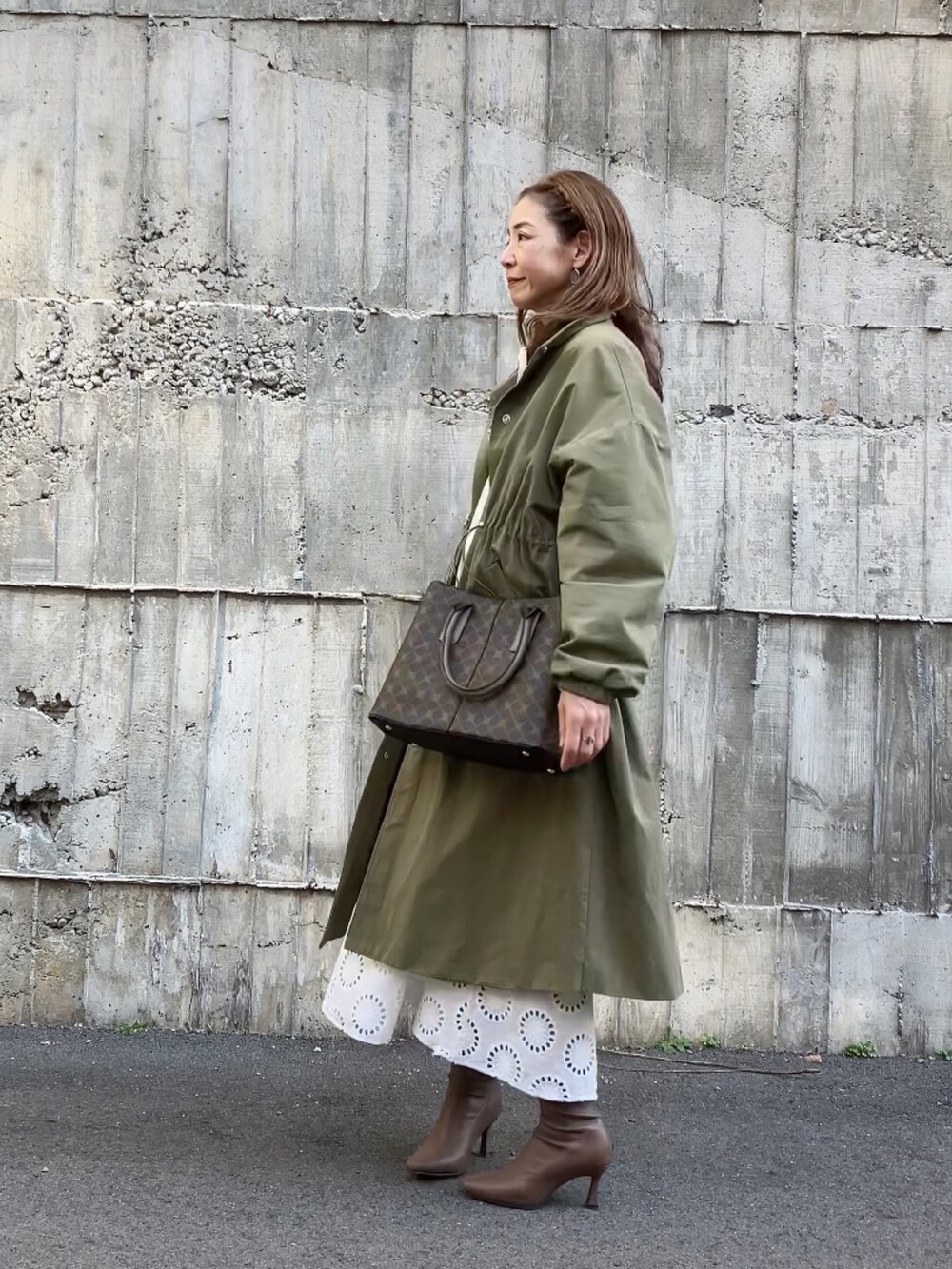 グリーン系のステンカラーコート、ブラウン系のハンドバッグ、ホワイト系のワンピース/ドレスを着用したレディースの冬コーディネートの3枚目の写真