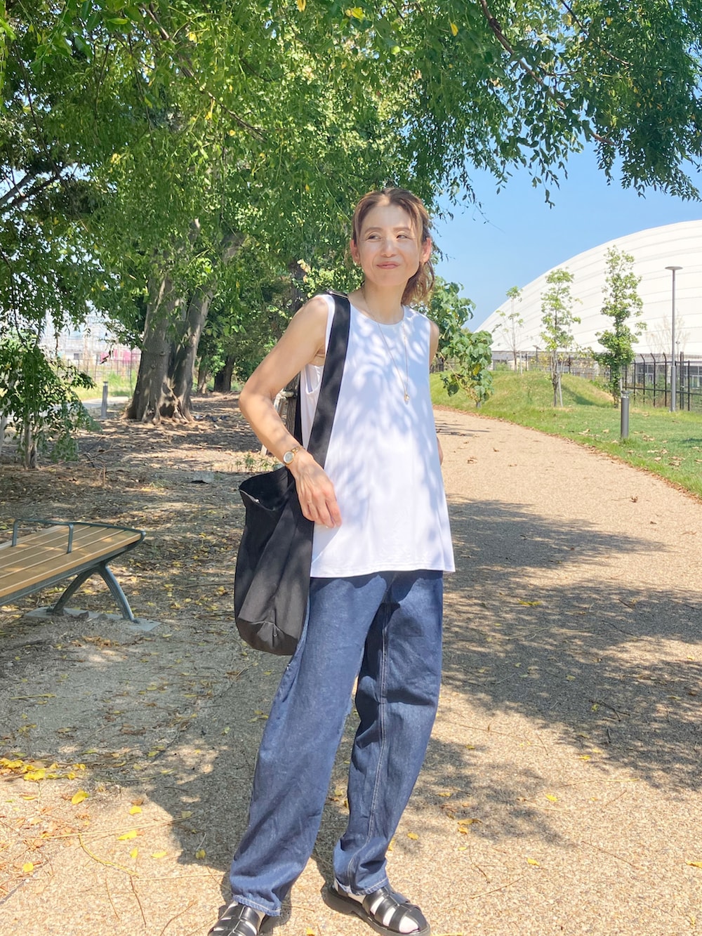 ホワイト系のタンクトップ、ブルー系のデニムパンツ、ブラック系のショルダーバッグを着用したレディースの夏コーディネートの2枚目の写真