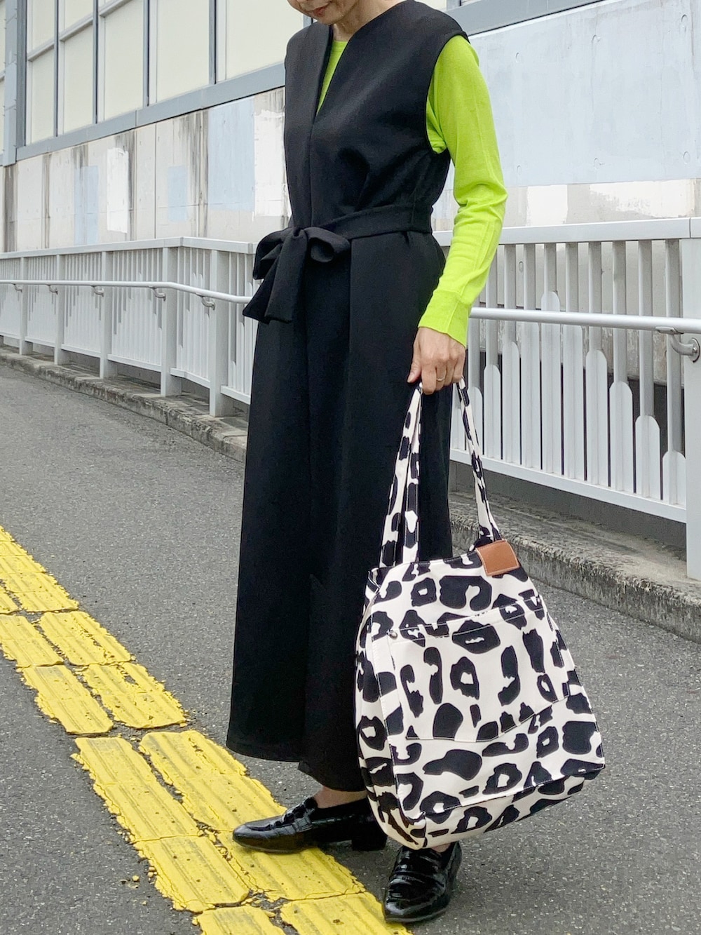 ブラック系のジャンパースカート、ベージュ系のトートバッグ、グリーン系のニット/セーターを着用したレディースの春コーディネートの2枚目の写真