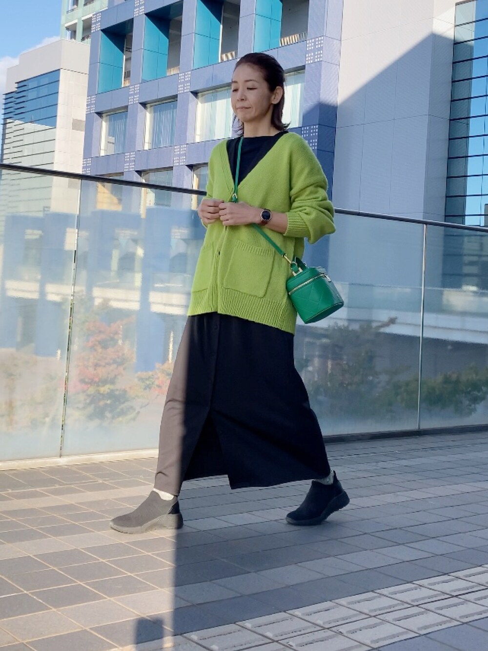 ブラック系のジャンパースカート、グリーン系のカーディガン/ボレロ、グリーン系のショルダーバッグを着用したレディースの秋コーディネートの2枚目の写真