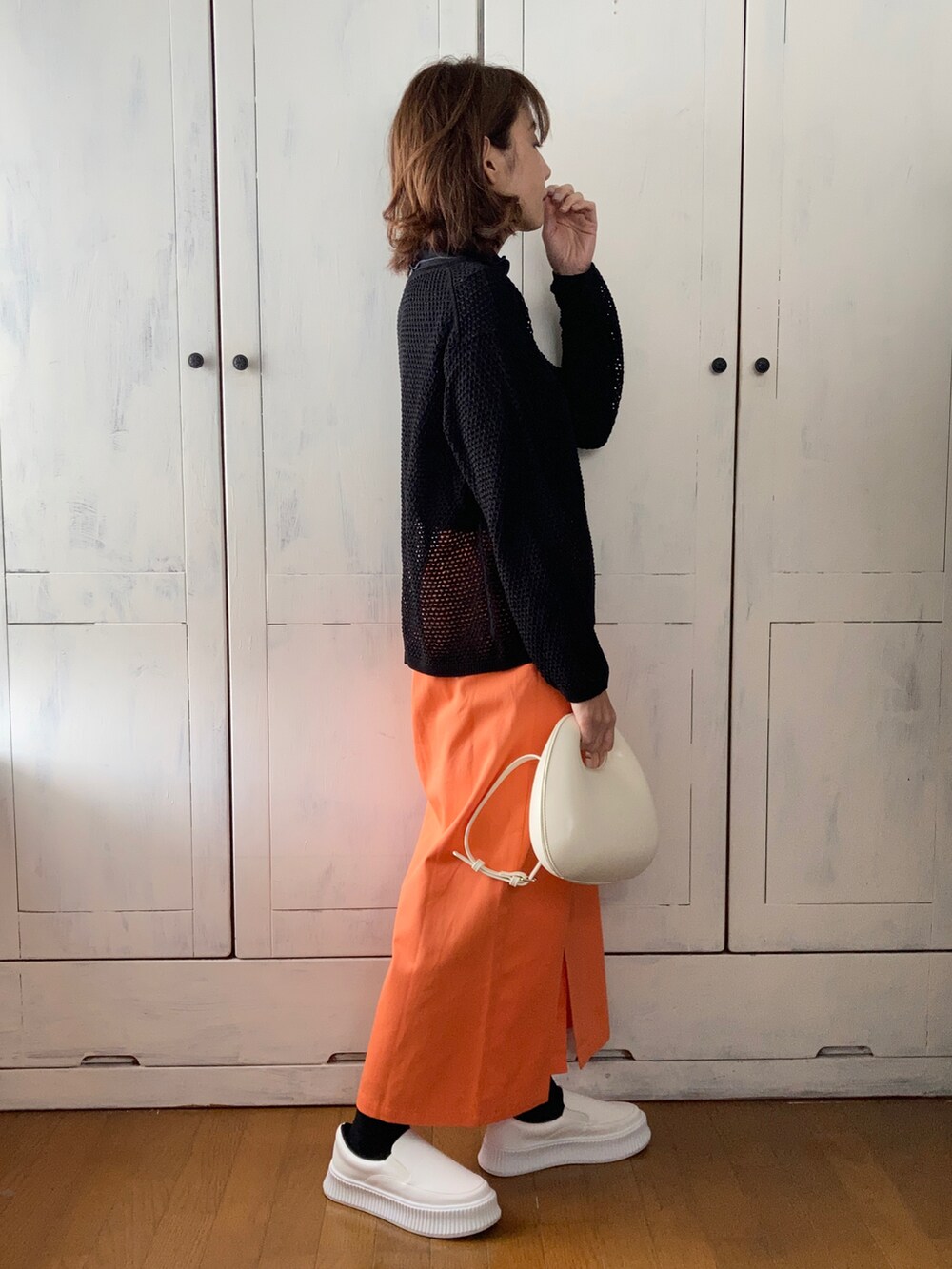オレンジ系のスカート、ホワイト系のバッグ、ホワイト系のスリッポンを着用したレディースの春コーディネートの2枚目の写真