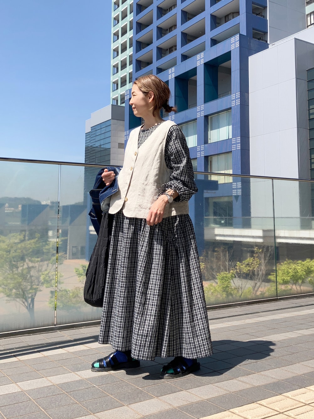 ベージュ系のベスト、ブルー系のデニムジャケット、ブラック系のワンピースを着用したレディースの春コーディネートの3枚目の写真