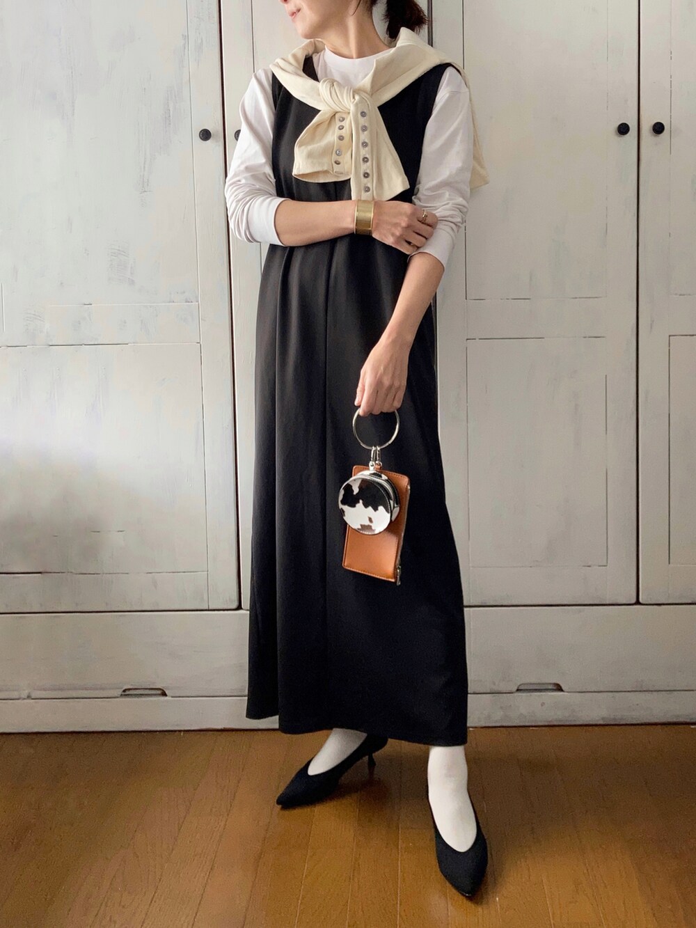 ブラック系のジャンパースカート、ホワイト系のカーディガン/ボレロ、ブラック系のパンプスを着用したレディースの春コーディネートの3枚目の写真