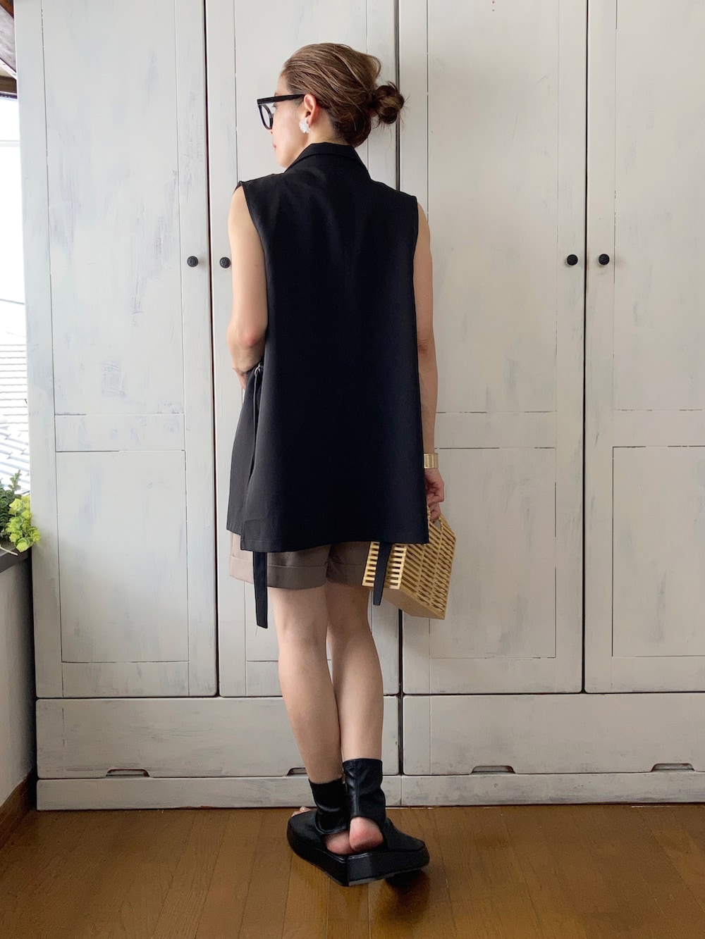 ブラック系のベスト、ベージュ系のパンツ、ベージュ系のかごバッグを着用したレディースの夏コーディネートの2枚目の写真