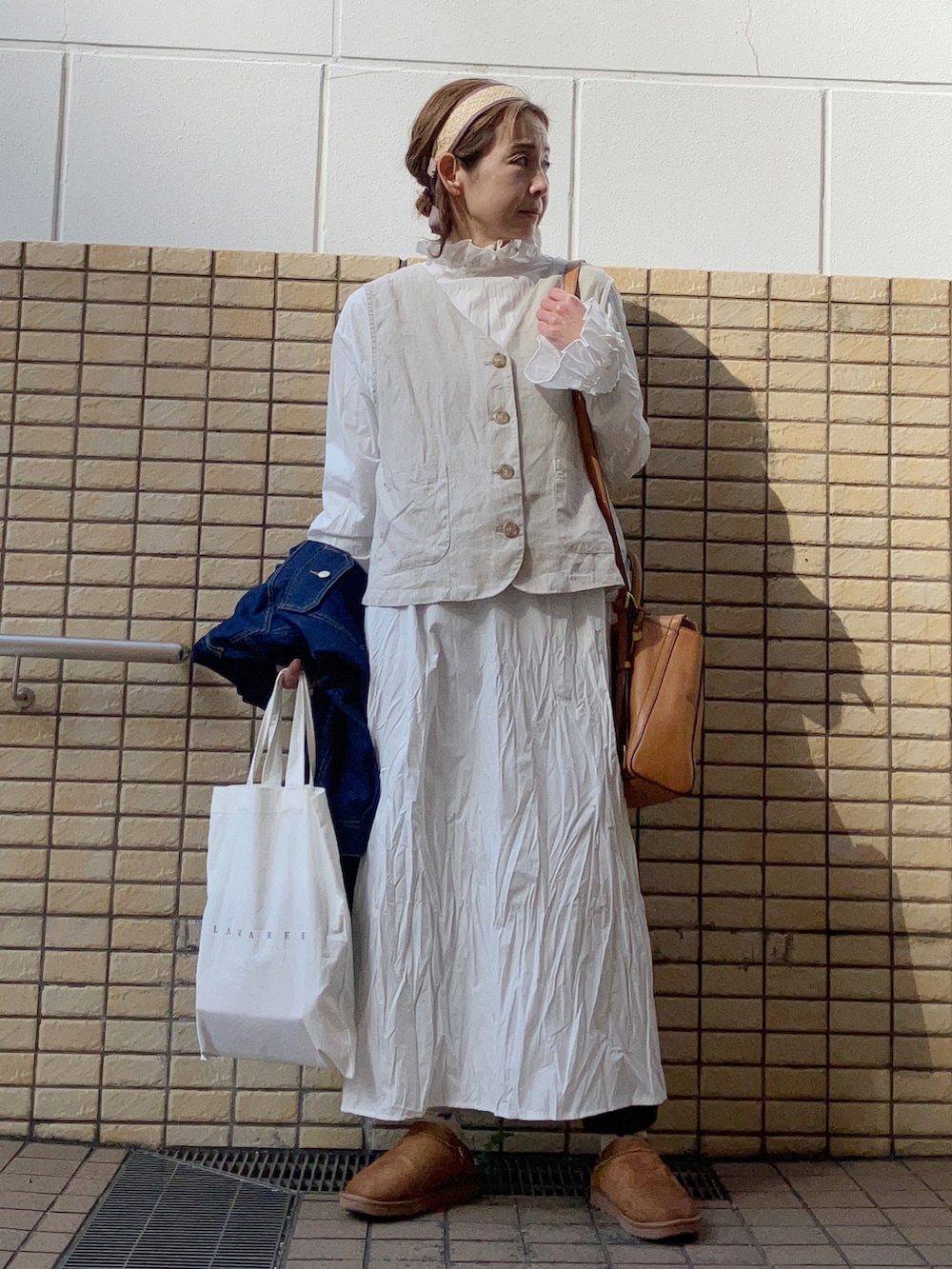 ベージュ系のベスト、ブルー系のデニムジャケット、ホワイト系のワンピースを着用したレディースの春コーディネートの3枚目の写真