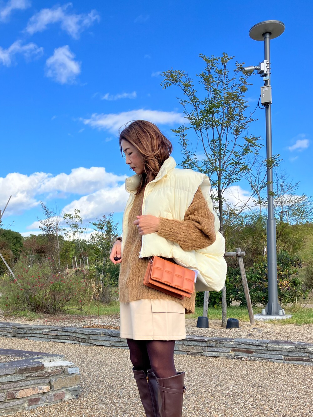 ホワイト系のダウンベスト、ブラウン系のニット/セーター、ホワイト系のスカートを着用したレディースの秋コーディネートの2枚目の写真