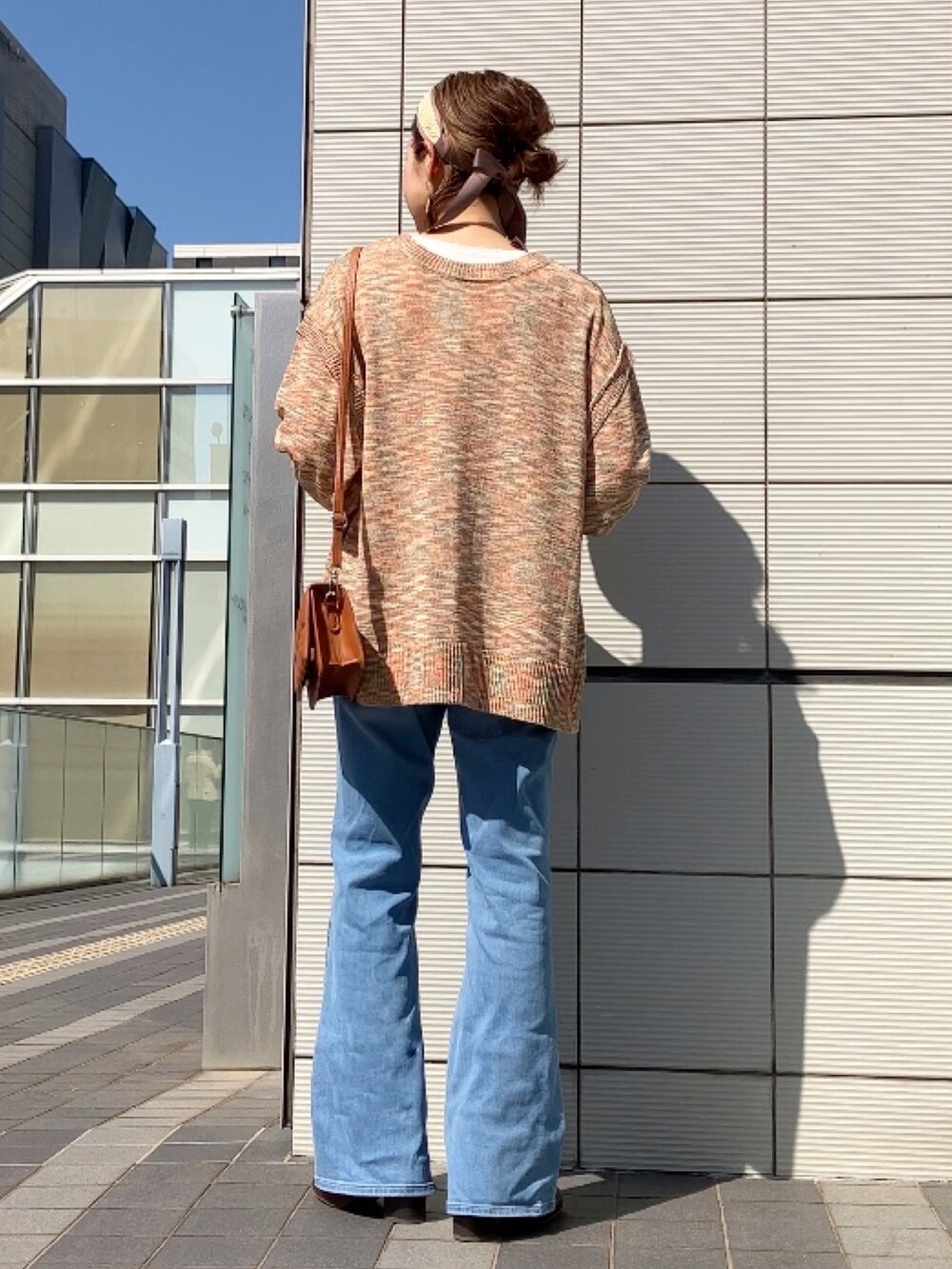 オレンジ系のカーディガン/ボレロ、ブラウン系のクラッチバッグ、ブルー系のデニムパンツを着用したレディースの春コーディネートの3枚目の写真