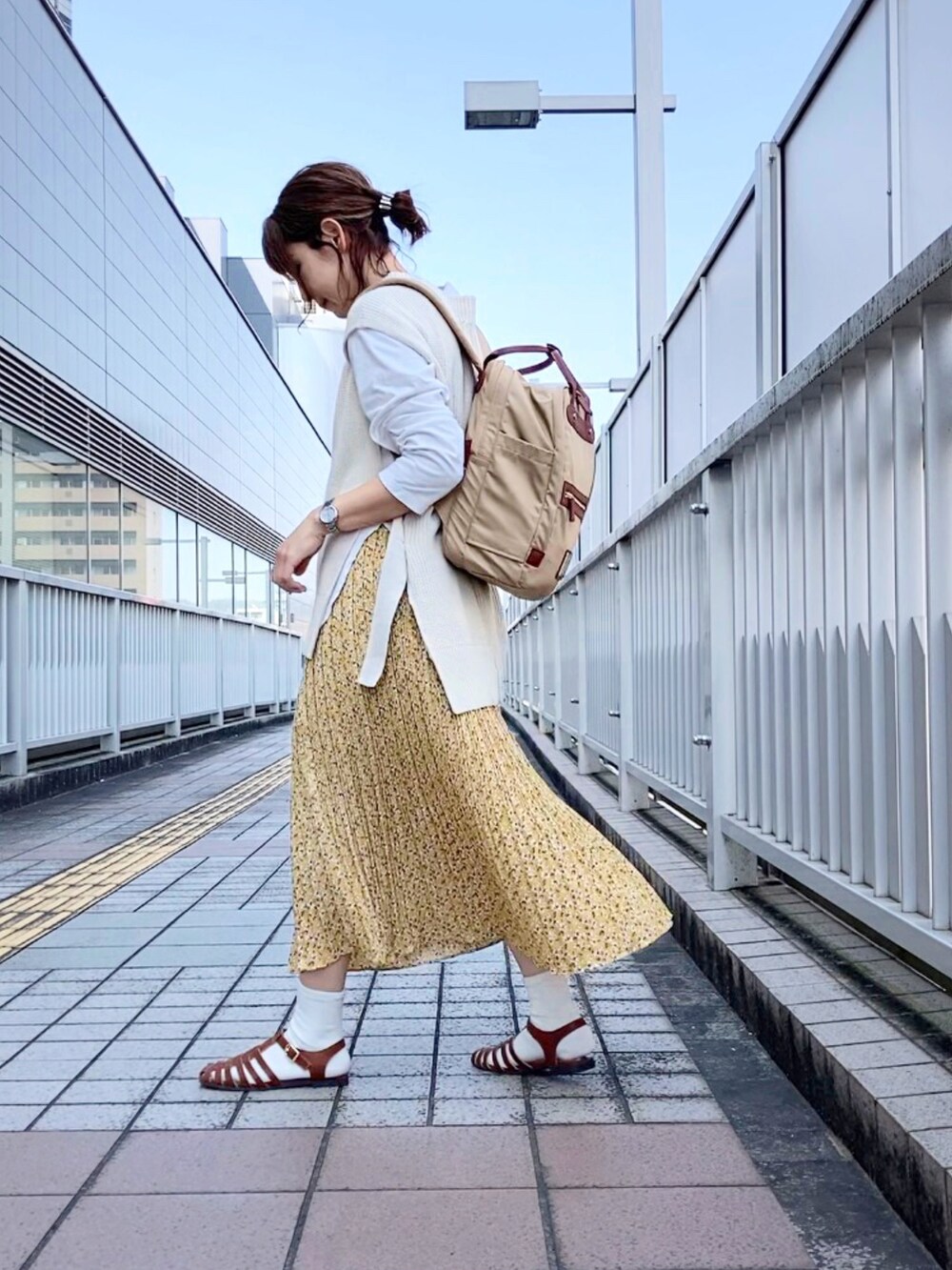 ホワイト系のベスト、イエロー系のスカート、ベージュ系のバックパック/リュックを着用したレディースの春コーディネートの2枚目の写真