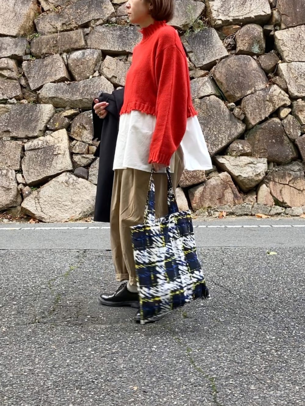 ブラック系のステンカラーコート、レッド系のニット/セーター、ブラック系のトートバッグを着用したレディースの秋コーディネートの3枚目の写真