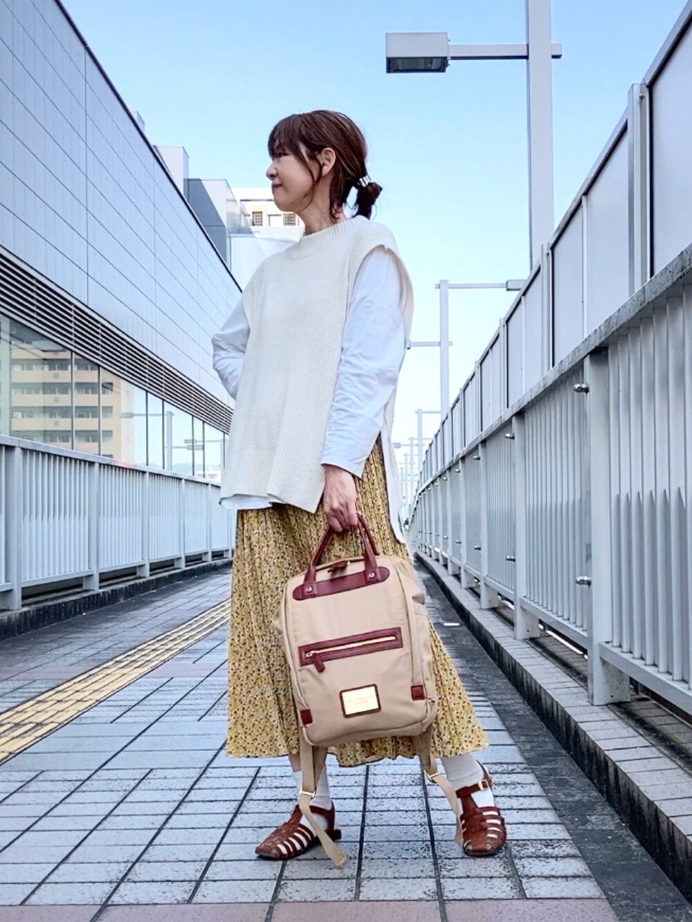 ホワイト系のベスト、イエロー系のスカート、ベージュ系のバックパック/リュックを着用したレディースの春コーディネートの3枚目の写真