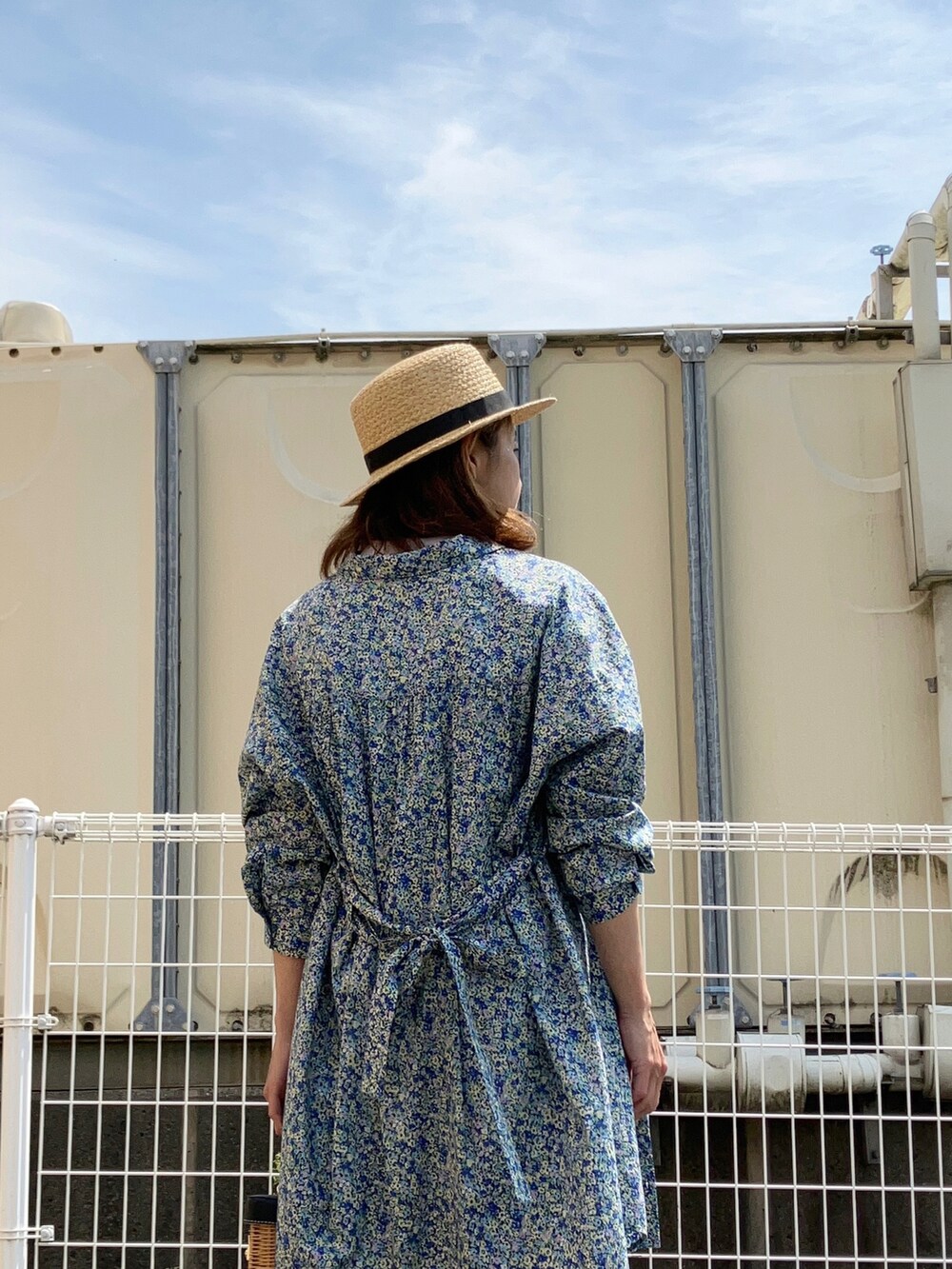 ブルー系のシャツワンピース、ブラウン系のかごバッグ、ブラック系のサンダルを着用したレディースの春コーディネートの2枚目の写真