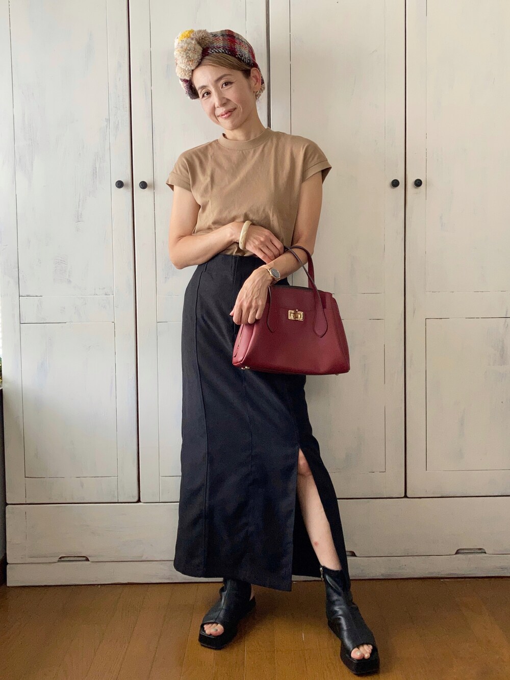 レッド系のハンドバッグ、ベージュ系のTシャツ/カットソー、ブラック系のスカートを着用したレディースの秋コーディネートの2枚目の写真