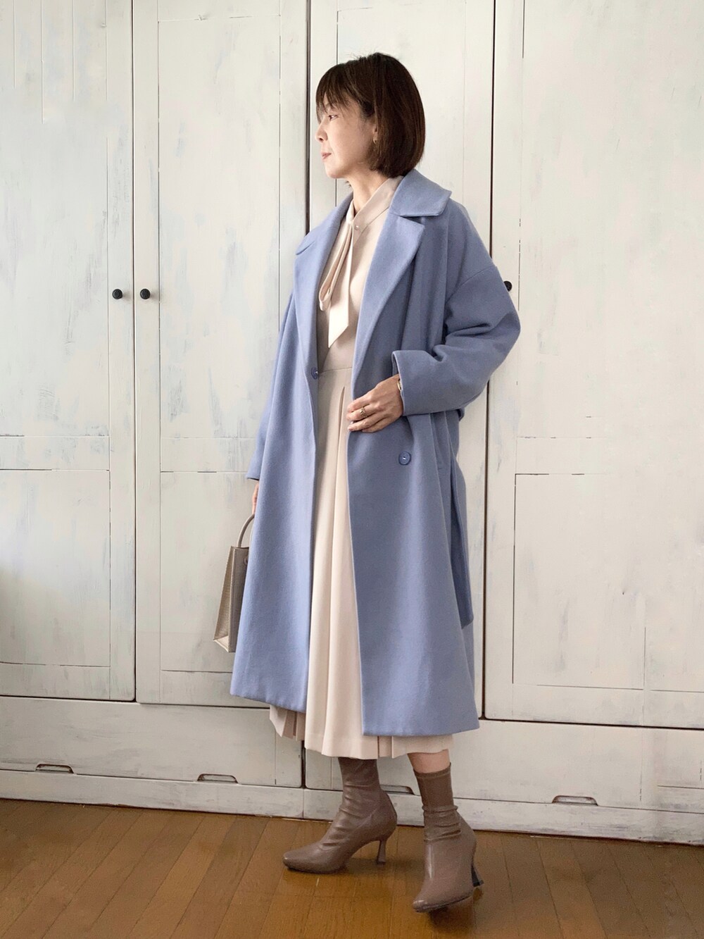 ベージュ系のワンピース、ブルー系のチェスターコート、ベージュ系のショルダーバッグを着用したレディースの冬コーディネートの4枚目の写真