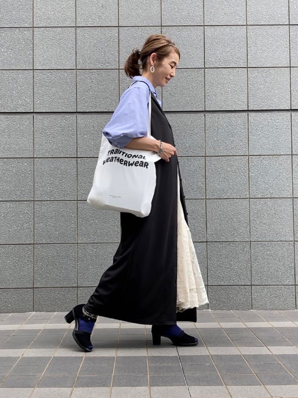 ブラック系のジャンパースカート、ブルー系のその他トップス、ホワイト系のスカートを着用したレディースの春コーディネートの3枚目の写真