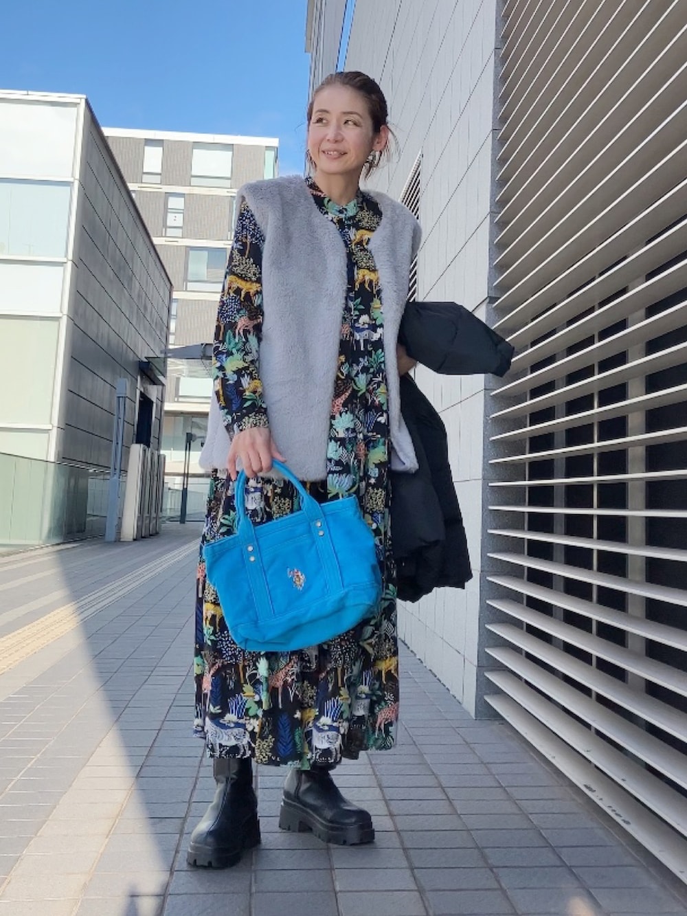 ブルー系のトートバッグ、ブラック系のワンピース、グレー系のベストを着用したレディースの冬コーディネートの3枚目の写真