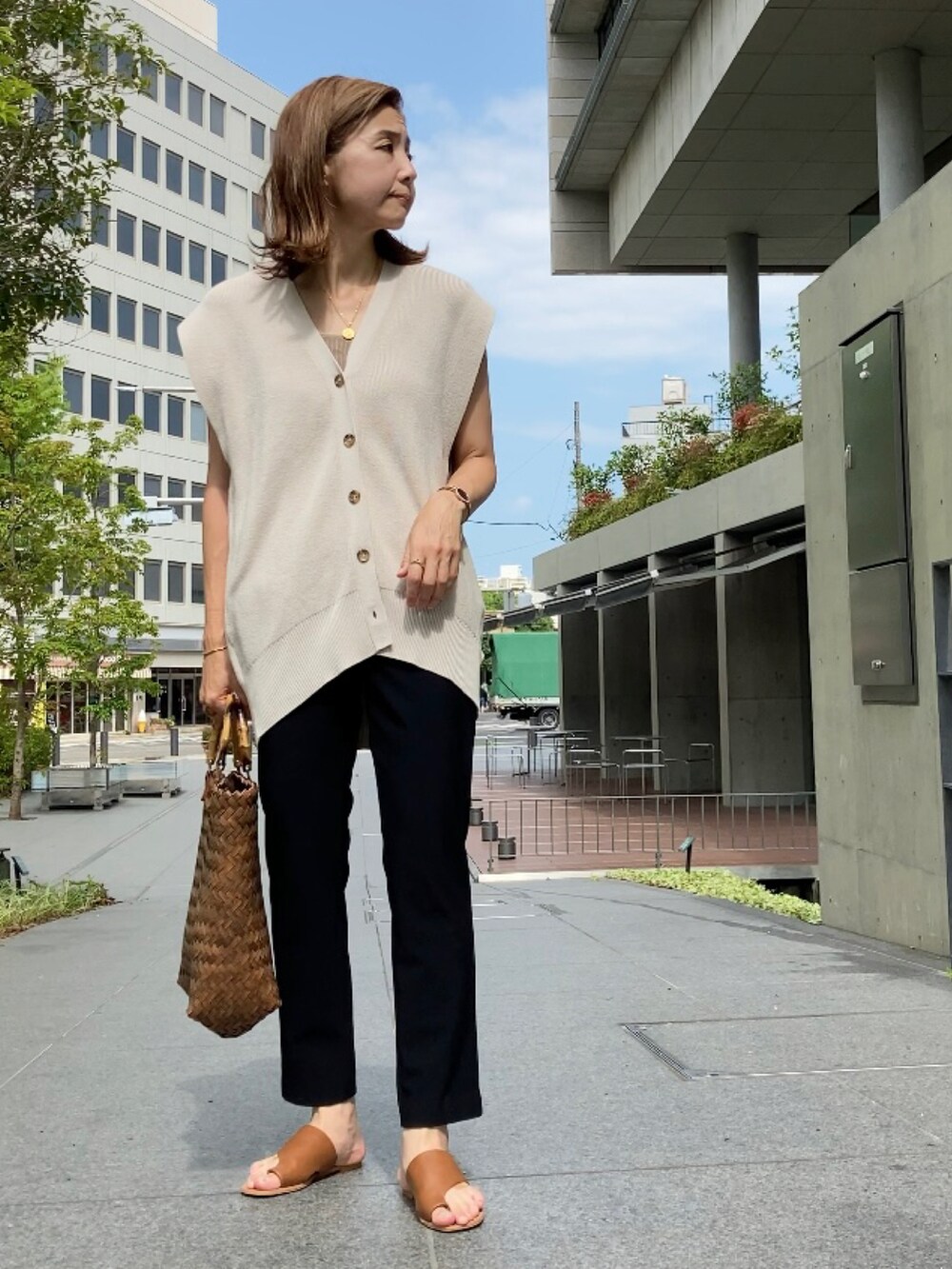 ベージュ系のベスト、ブラック系のパンツ、ブラウン系のかごバッグを着用したレディースの夏コーディネートの2枚目の写真