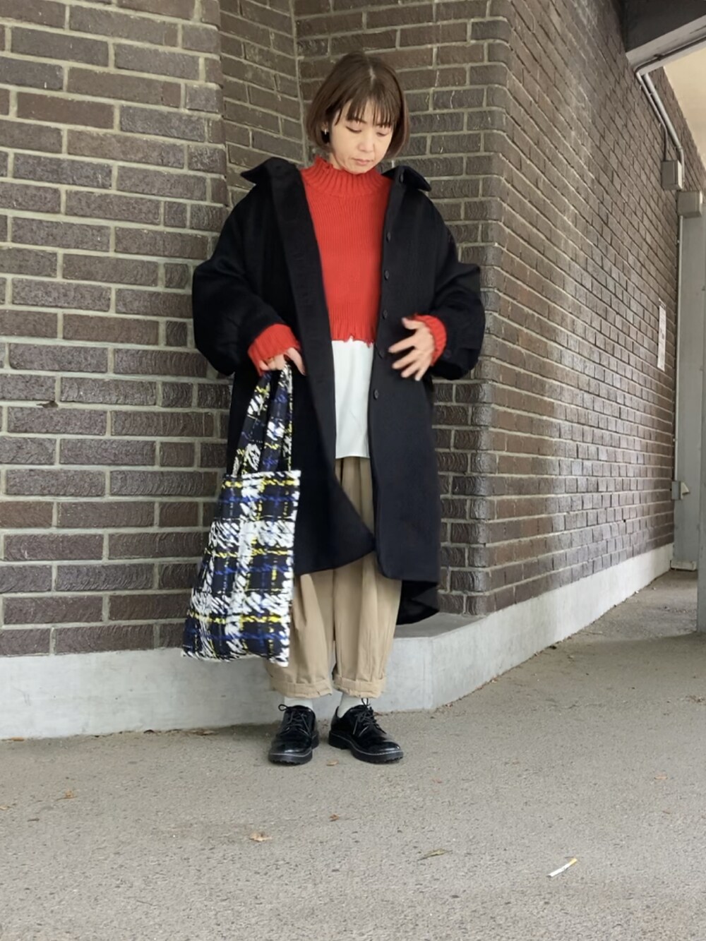 ブラック系のステンカラーコート、レッド系のニット/セーター、ブラック系のトートバッグを着用したレディースの秋コーディネートの4枚目の写真
