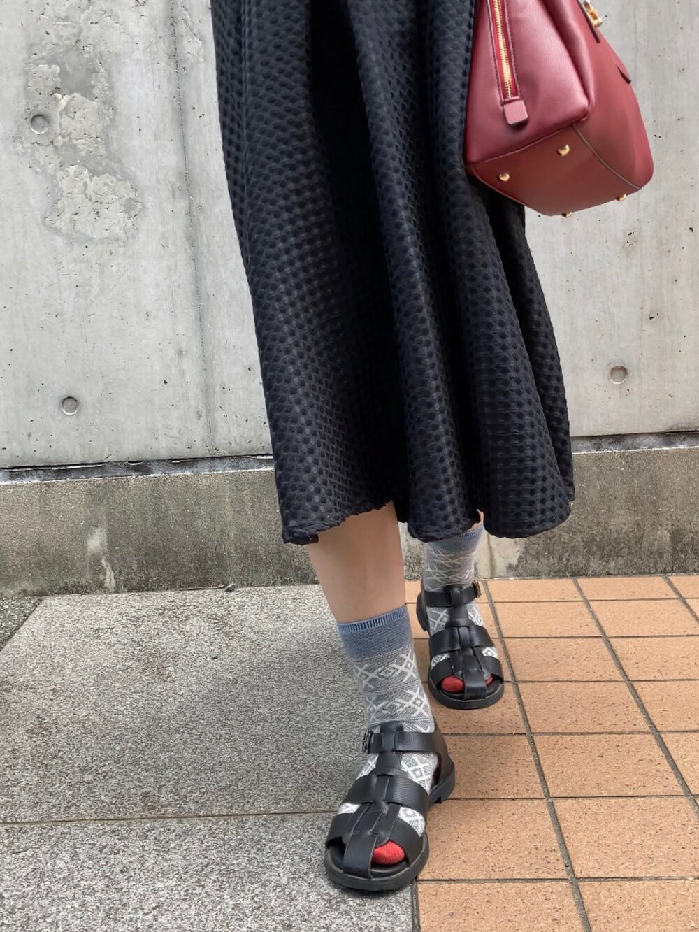 ブラック系のニット/セーター、ブラック系のスカート、レッド系のハンドバッグを着用したレディースの夏コーディネートの3枚目の写真