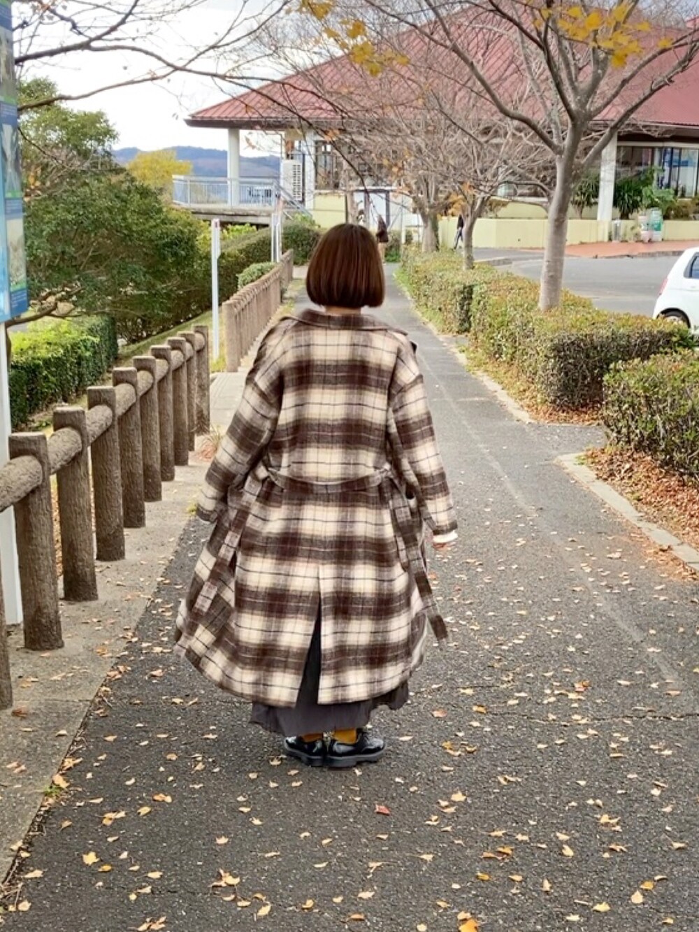 ブラウン系のチェスターコート、ブラック系のハンドバッグ、ホワイト系のニット/セーターを着用したレディースの冬コーディネートの2枚目の写真