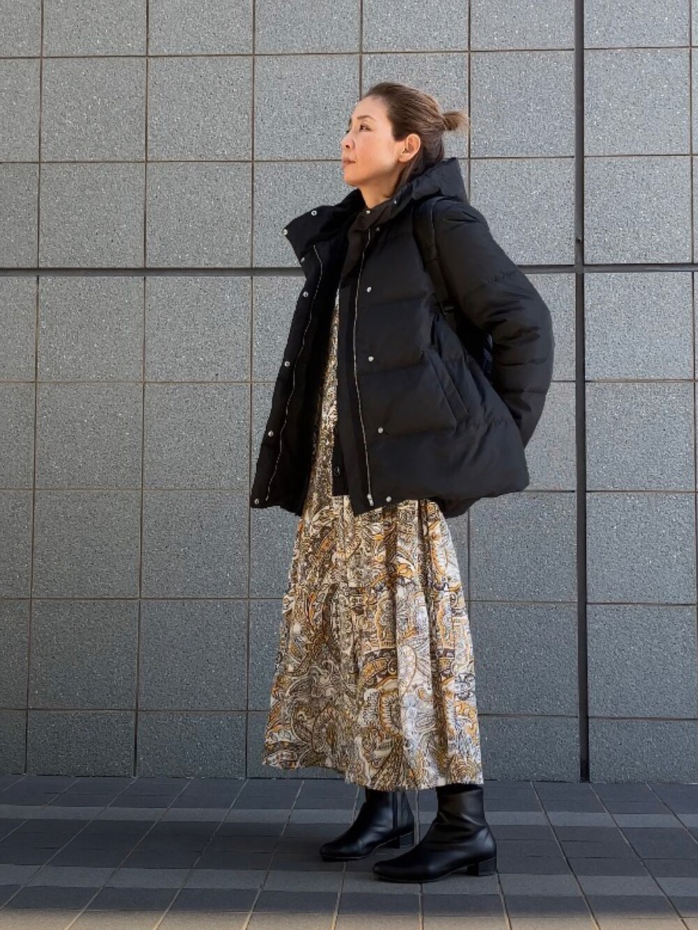 ブラック系のダウンジャケット/コート、イエロー系のワンピース、ブラック系のブーツを着用したレディースの冬コーディネートの4枚目の写真