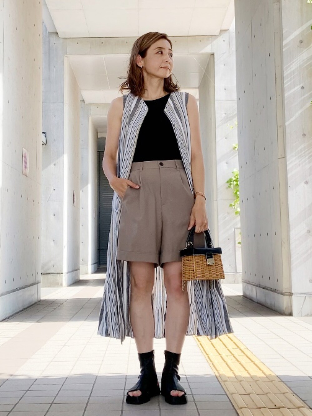 ベージュ系のパンツ、ホワイト系のワンピース、ブラック系のブーツを着用したレディースの夏コーディネートの2枚目の写真