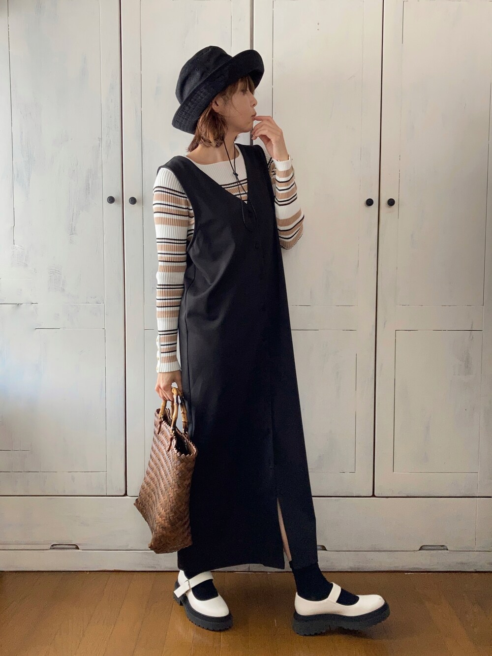 ブラック系のジャンパースカート、ホワイト系のニット/セーター、ブラウン系のかごバッグを着用したレディースの春コーディネートの3枚目の写真