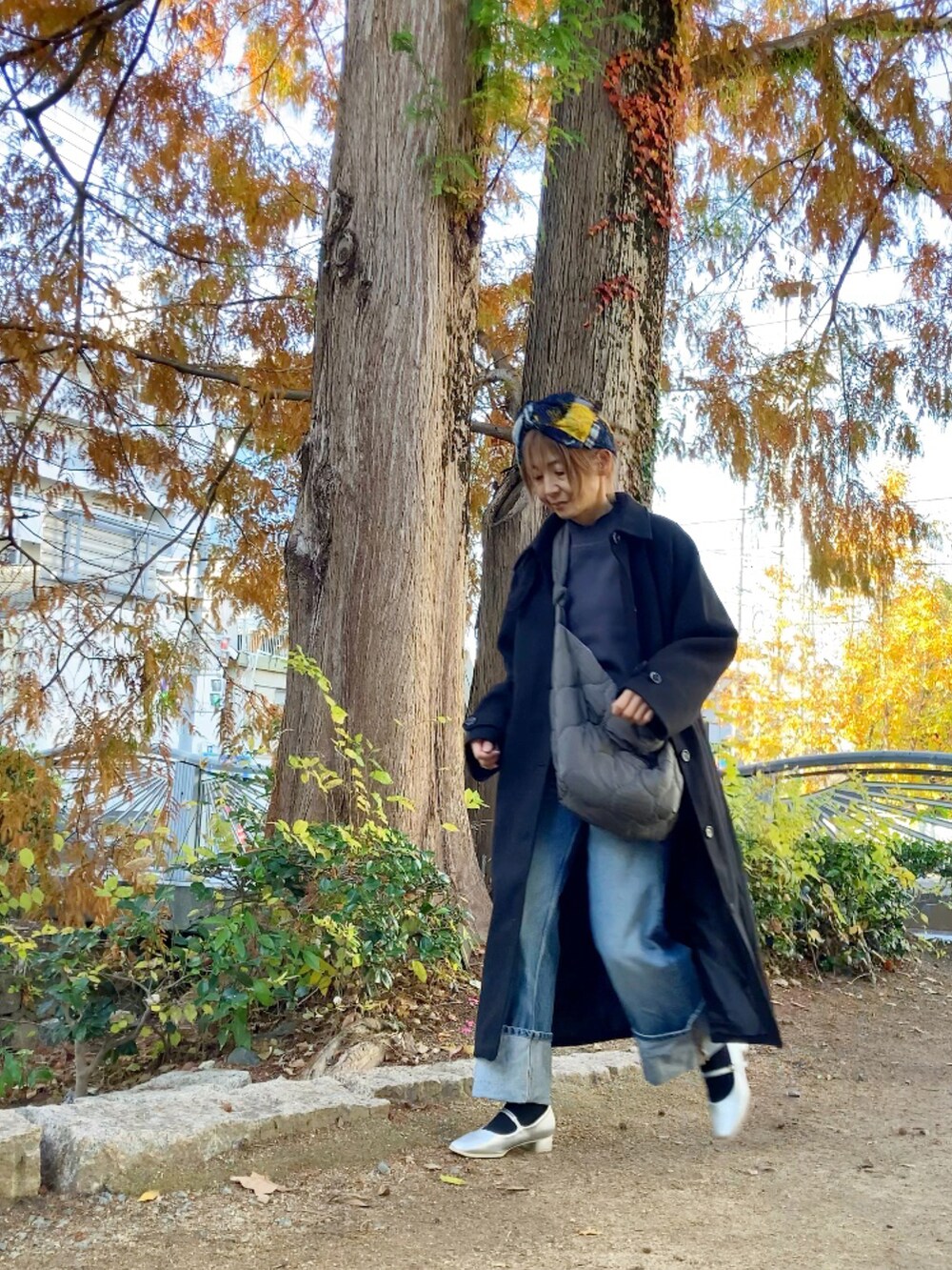 ブラック系のステンカラーコート、グレー系のニット/セーター、グレー系のショルダーバッグを着用したレディースの秋コーディネートの2枚目の写真