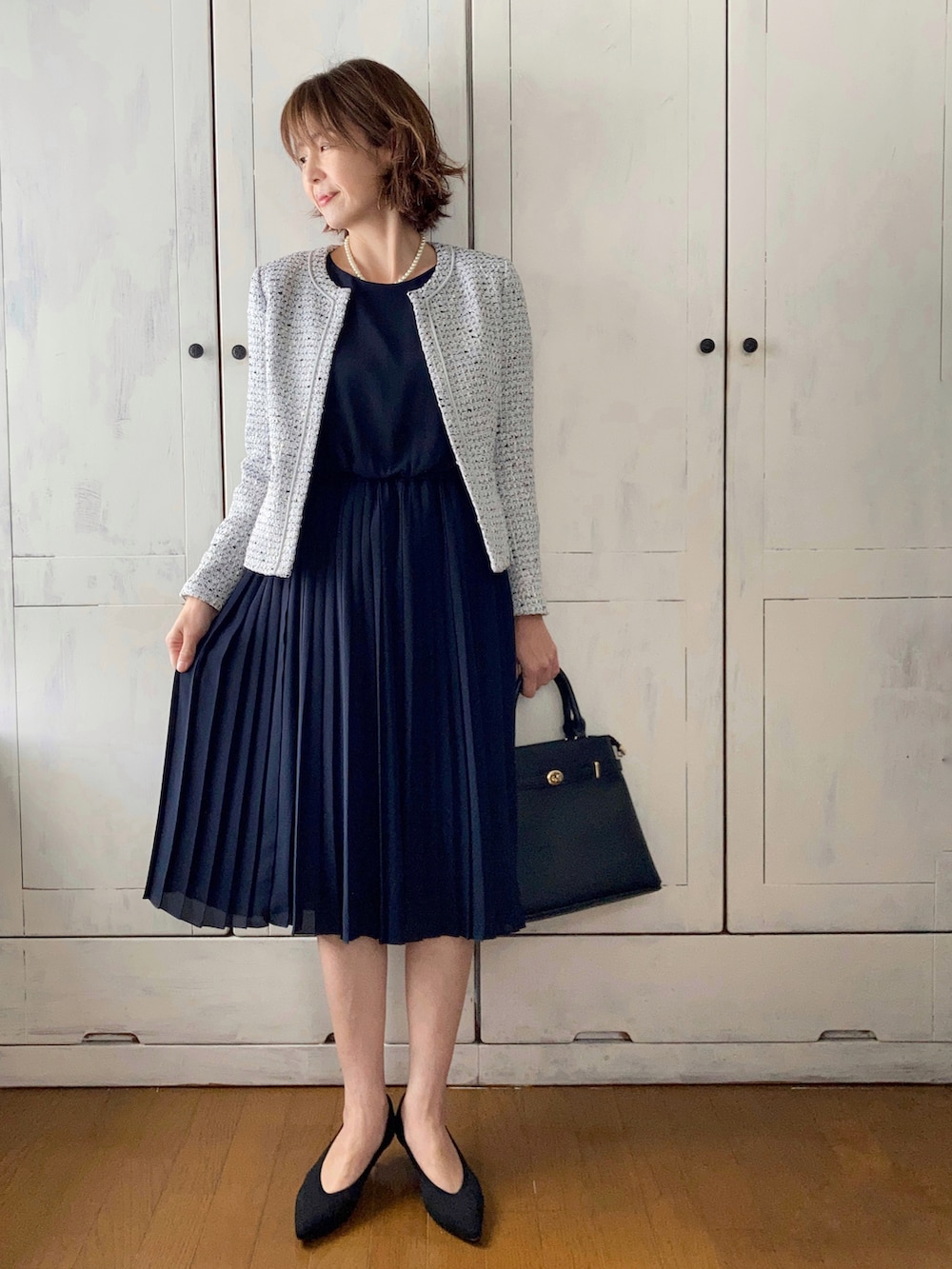 ブルー系のスーツセット、ブラック系のハンドバッグ、ブラック系のパンプスを着用したレディースの冬コーディネートの2枚目の写真