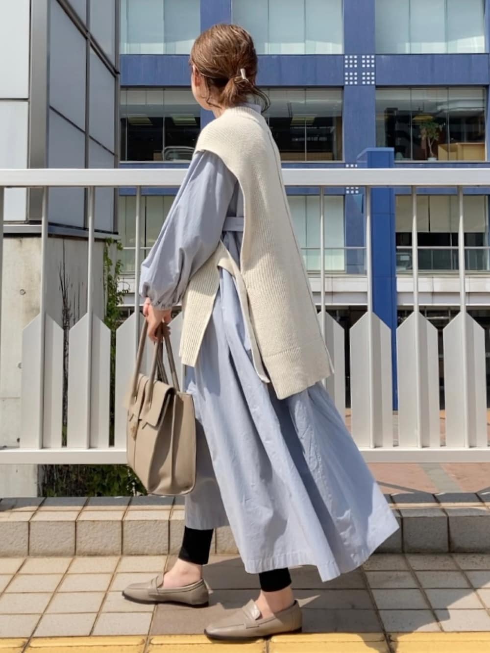 ホワイト系のベスト、ブルー系のシャツワンピース、ベージュ系のビジネスバッグを着用したレディースの春コーディネートの3枚目の写真