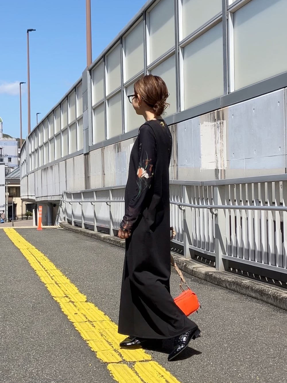 ブラック系のジャンパースカート、ブラック系のTシャツ/カットソー、オレンジ系のショルダーバッグを着用したレディースの春コーディネートの2枚目の写真