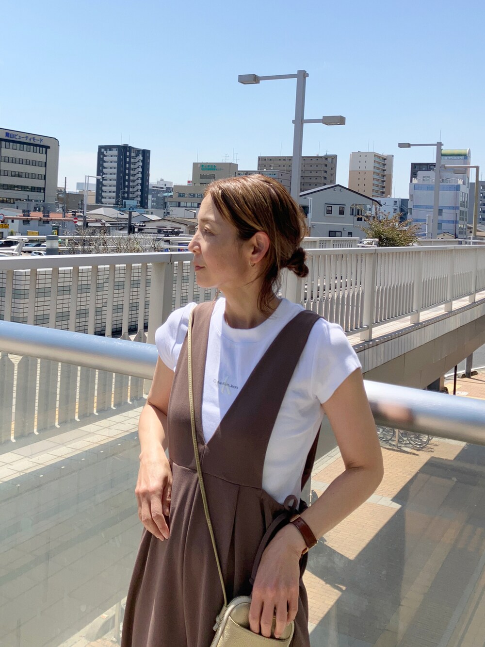 ブラウン系のサロペット/オーバーオール、ホワイト系のTシャツ/カットソー、ゴールド系のバッグを着用したレディースの春コーディネートの2枚目の写真