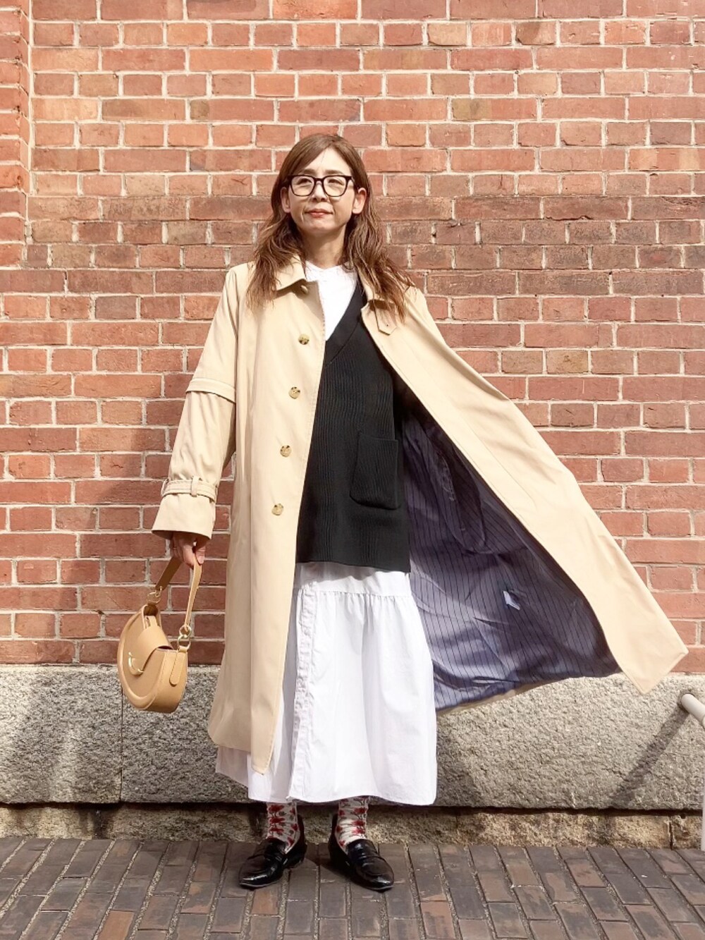 ベージュ系のトレンチコート、ベージュ系のハンドバッグ、ブラック系のシューズを着用したレディースの春コーディネートの2枚目の写真