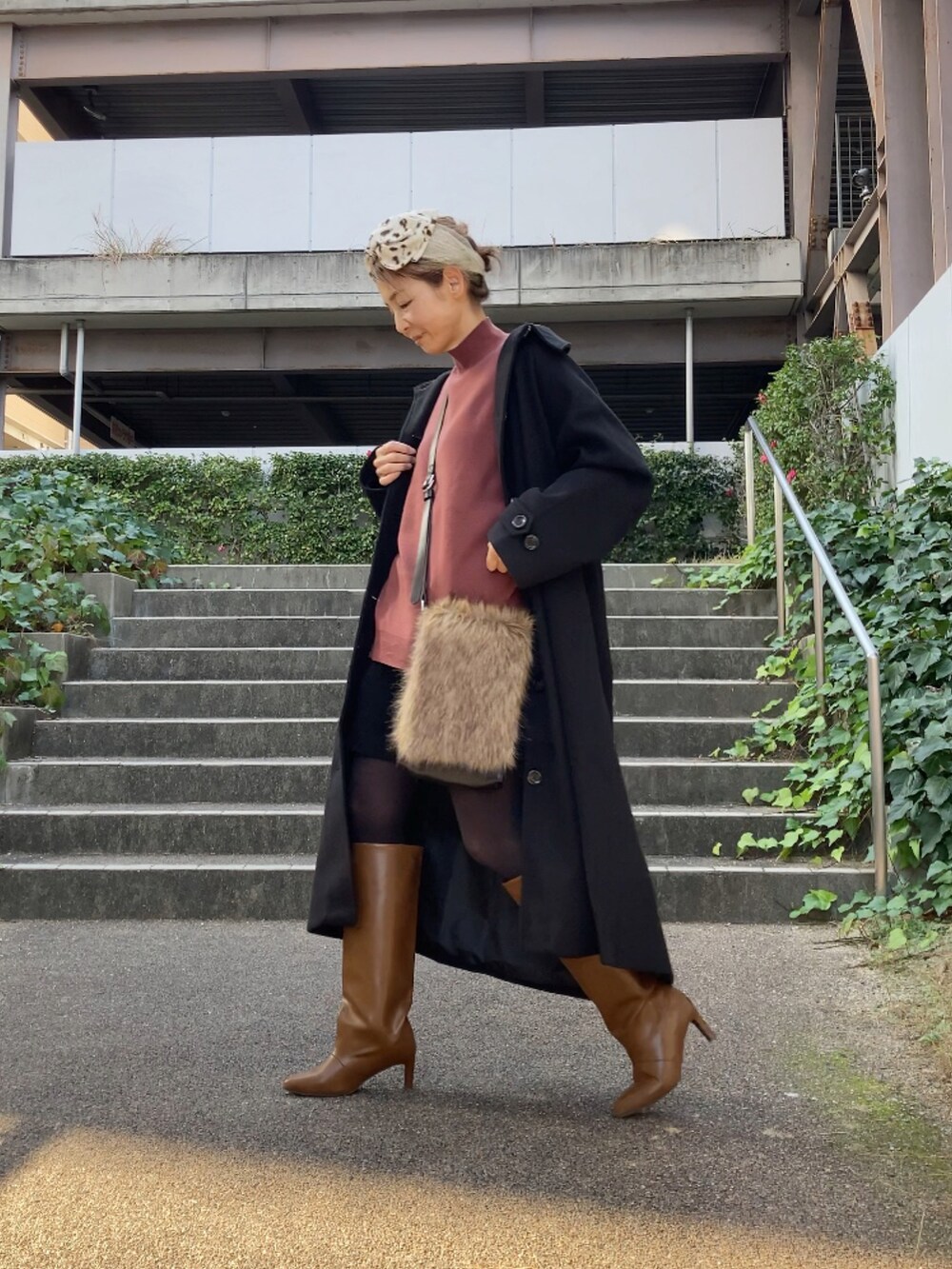 ブラック系のステンカラーコート、ブラウン系のニット/セーター、ブラック系のパンツを着用したレディースの冬コーディネートの2枚目の写真