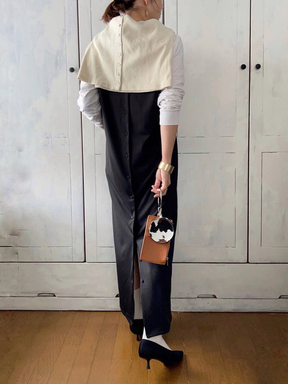 ブラック系のジャンパースカート、ホワイト系のカーディガン/ボレロ、ブラック系のパンプスを着用したレディースの春コーディネートの2枚目の写真